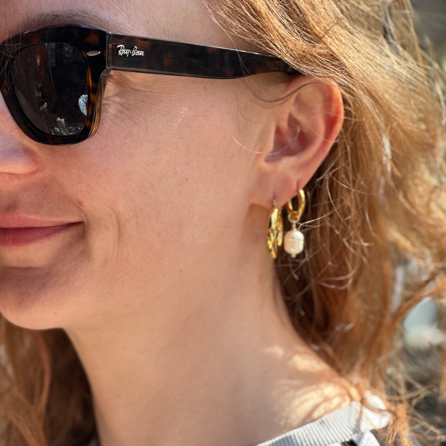 Close-up of a person wearing sunglasses with gold hoop pearl earrings.