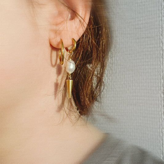 Gold hoop earrings with a pearl accent worn by a person against a neutral background