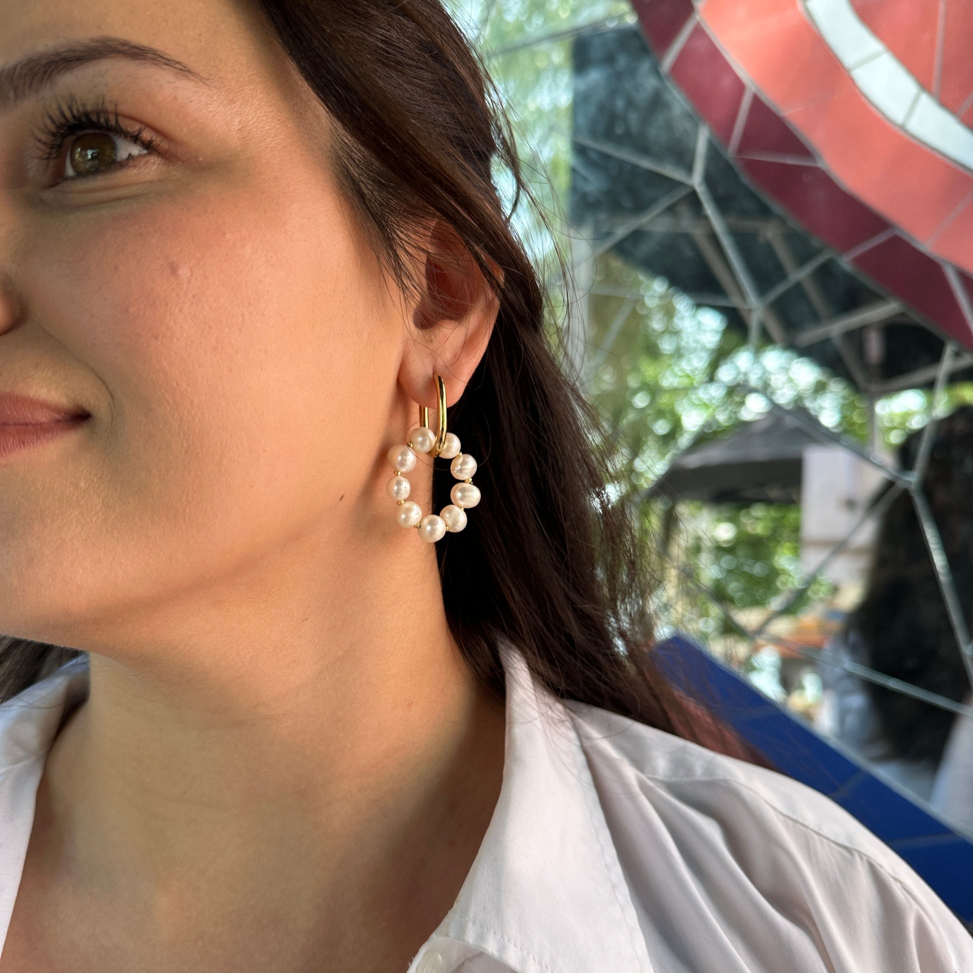 Close-up of a person wearing handmade pearl earrings with a blurred outdoor background