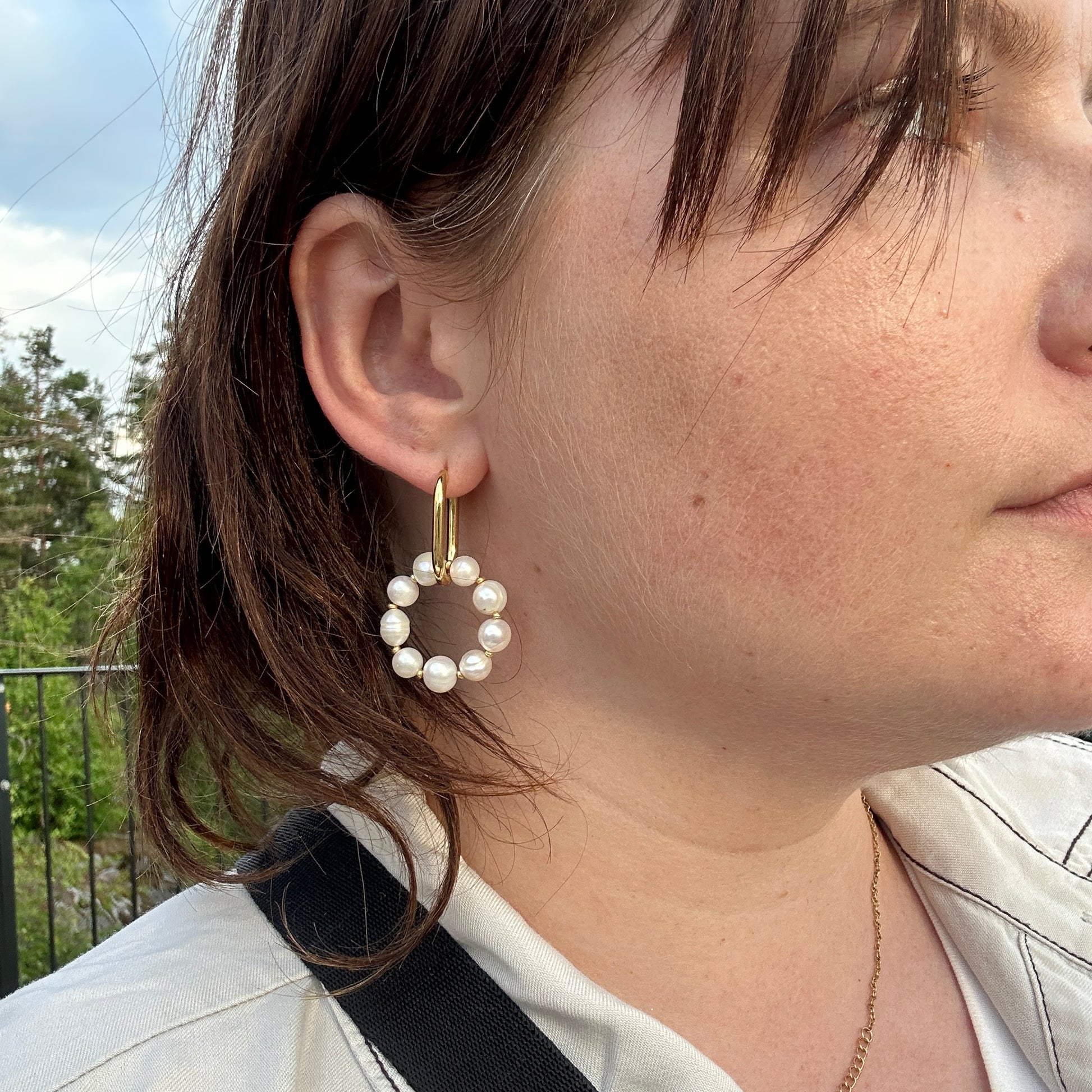 Close-up of a person wearing a gold hoop earring with pearl beads outdoors.