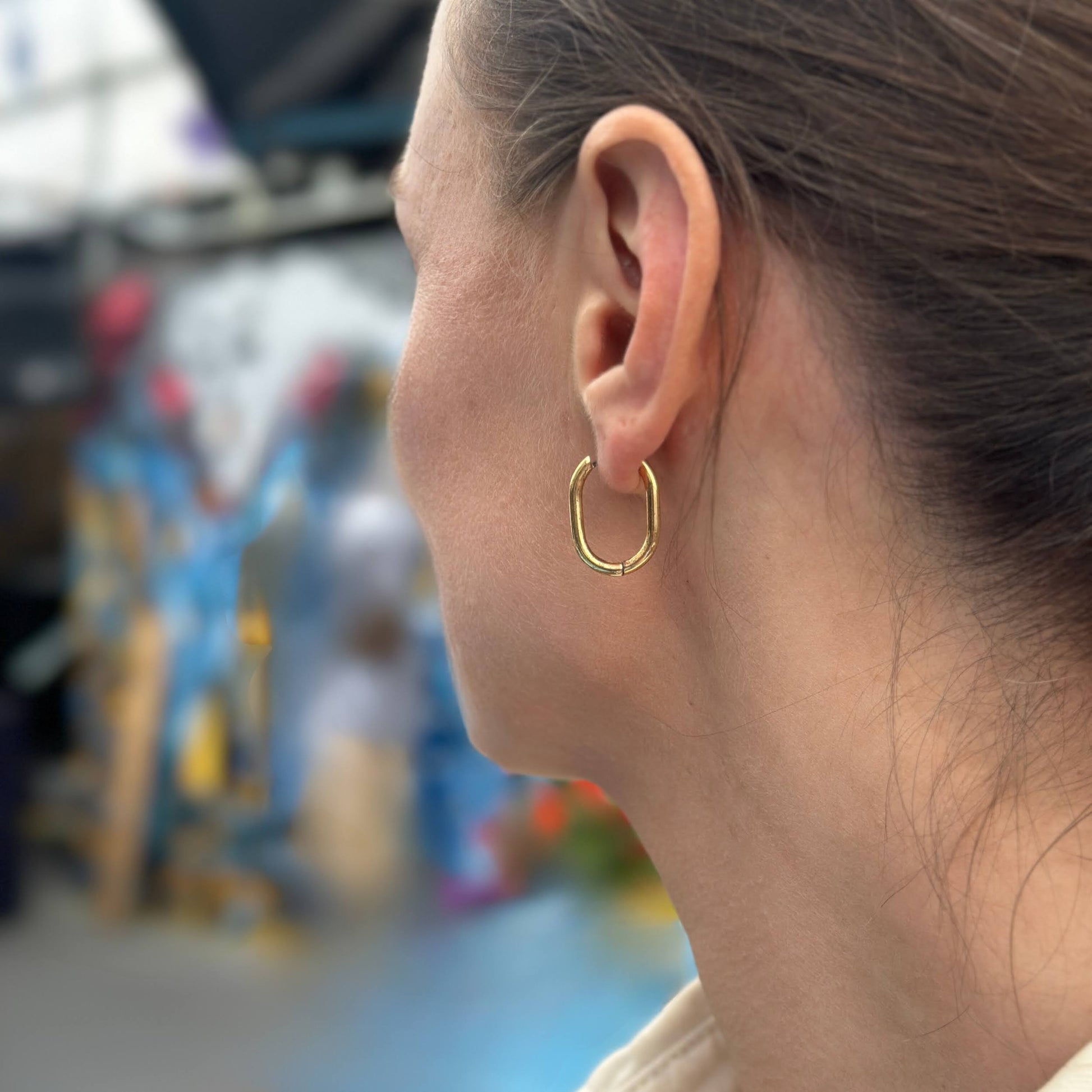 Close-up of a person wearing a gold hoop earring with a blurred background