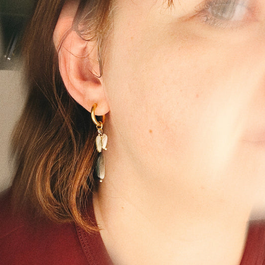 Close-up of a person wearing a gold earring with shells and a red shirt.