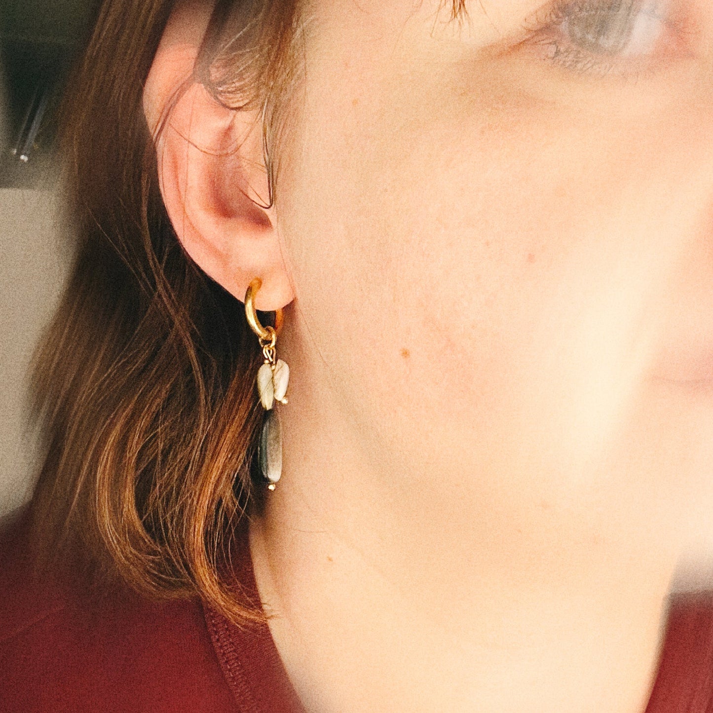Close-up of a person wearing a gold earring with shells and a red shirt.