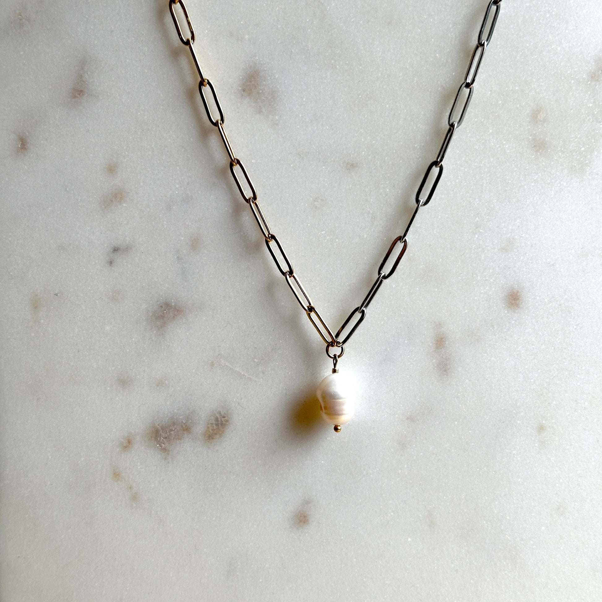 Handmade chain necklace, half gold and half silve,r with a pendant on a marble surface