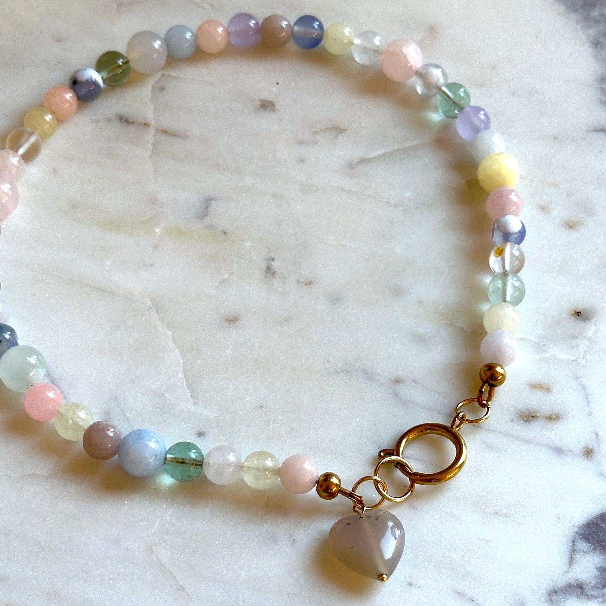 Handmade beaded necklace with colourful stones and a heart pendant made of agate on a marble surface