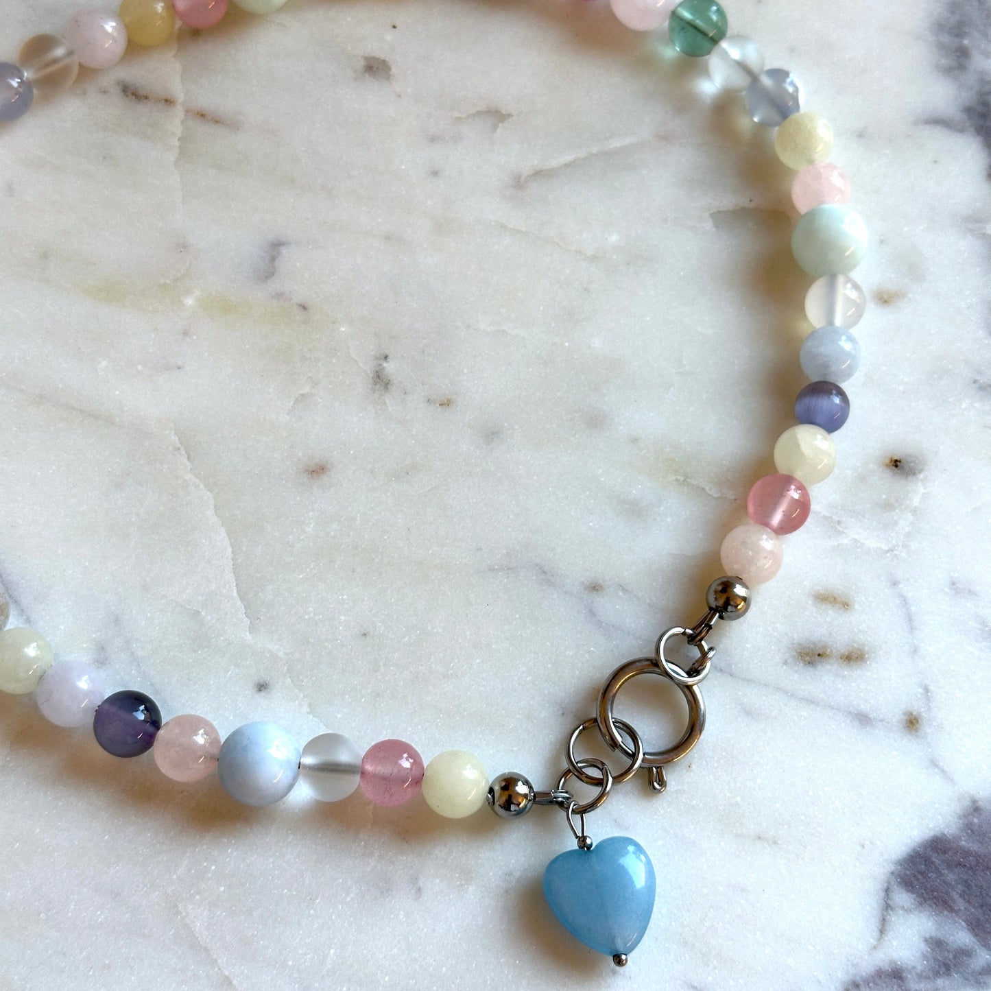 Handmade beaded necklace with colourful stones and a heart pendant made of aquamarine on a marble surface