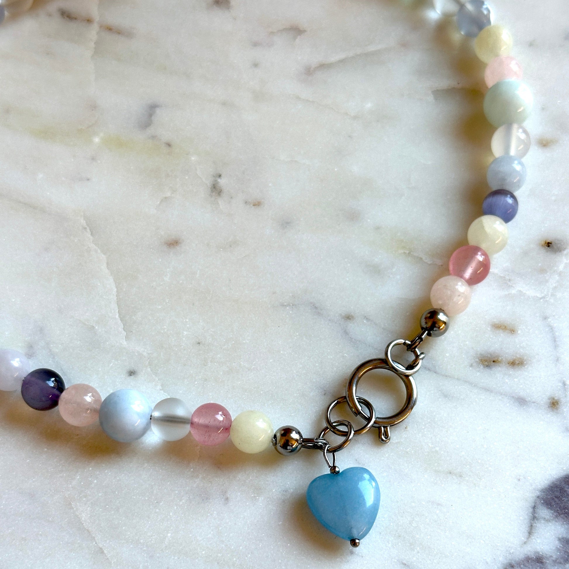 Handmade beaded necklace with colourful stones and a heart pendant made of aquamarine on a marble surface