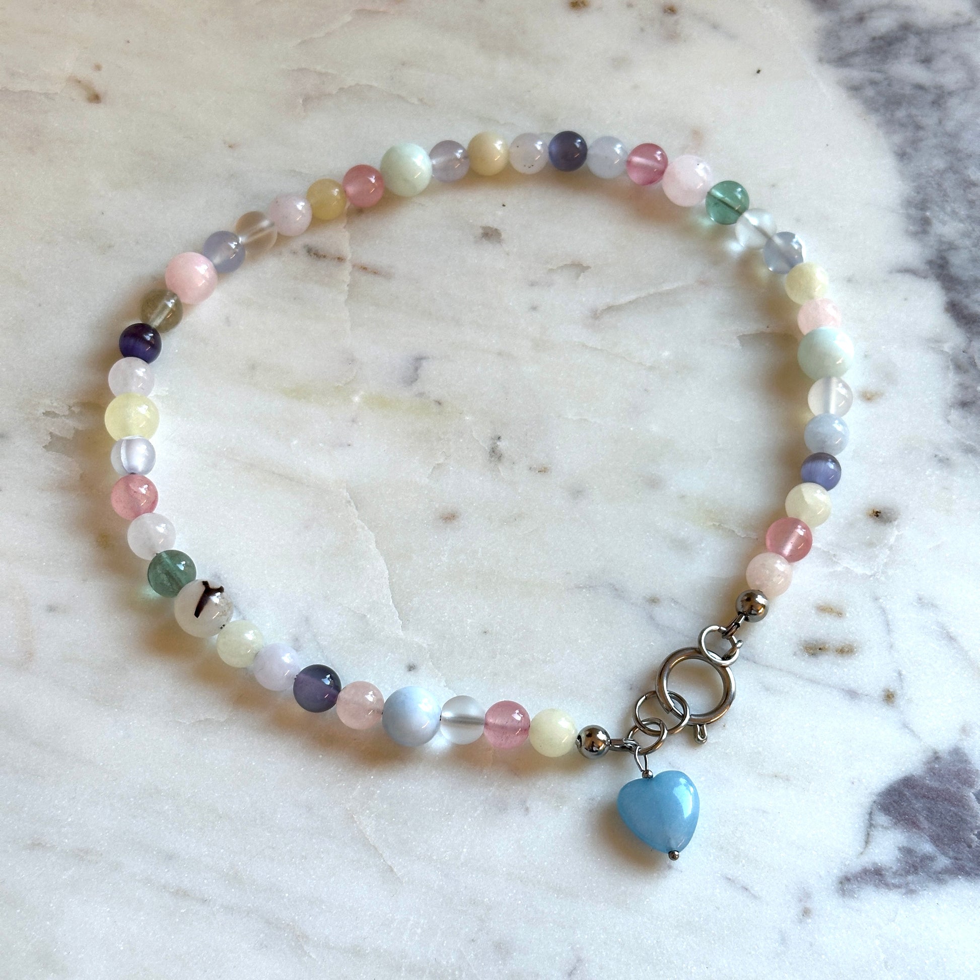 Handmade beaded necklace with colourful stones and a heart pendant made of aquamarine on a marble surface