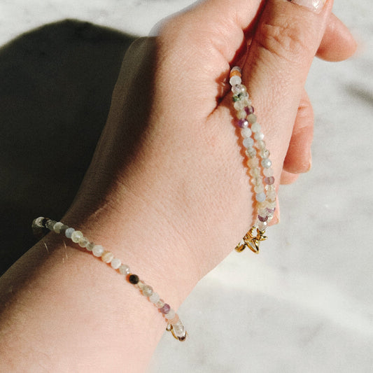 Hand wearing a beaded bracelet on a neutral background