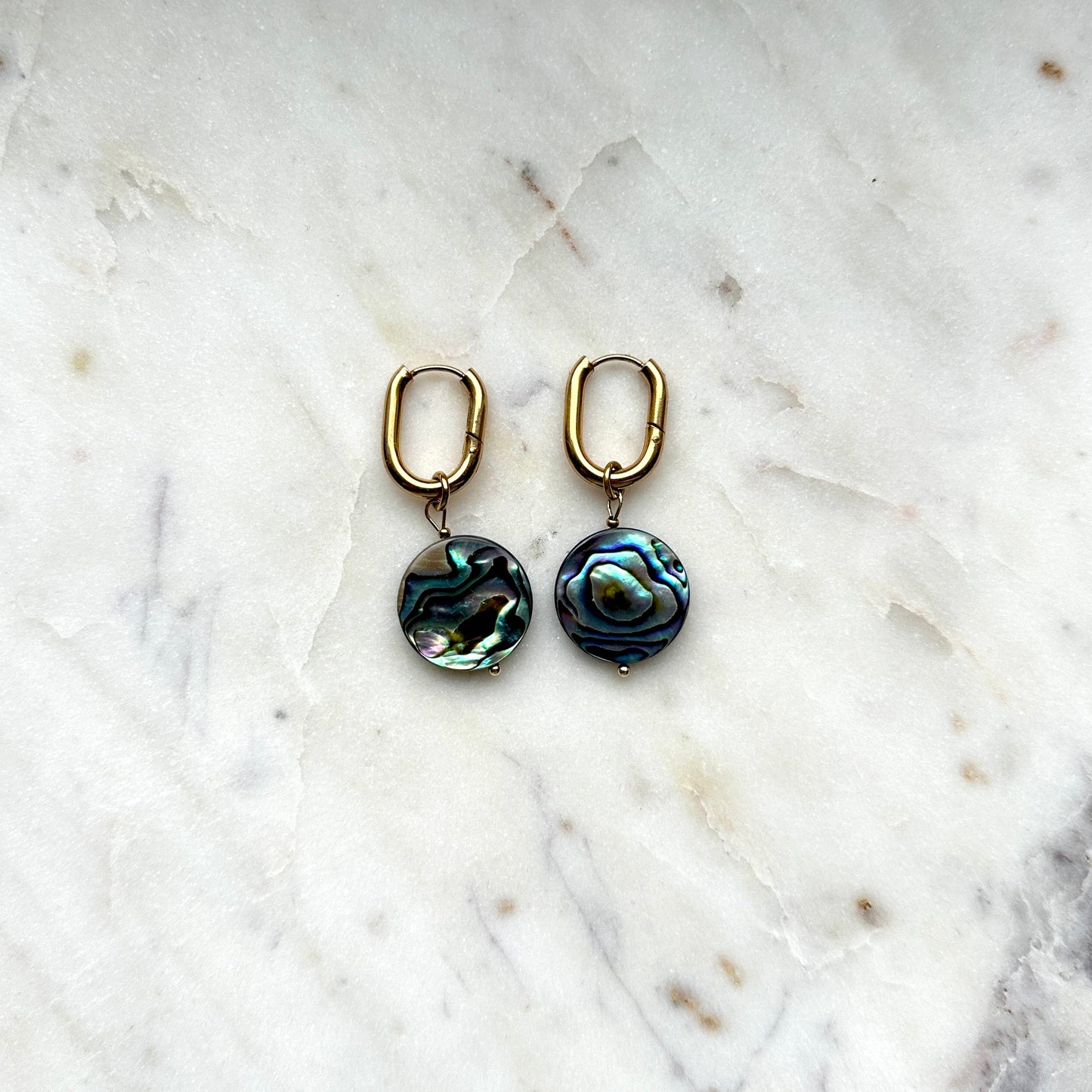 handmade earrings of abalone shell lying on a white marble background