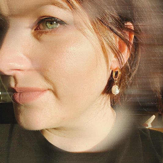 Close-up of a person wearing gold hoop earrings with a blurred background