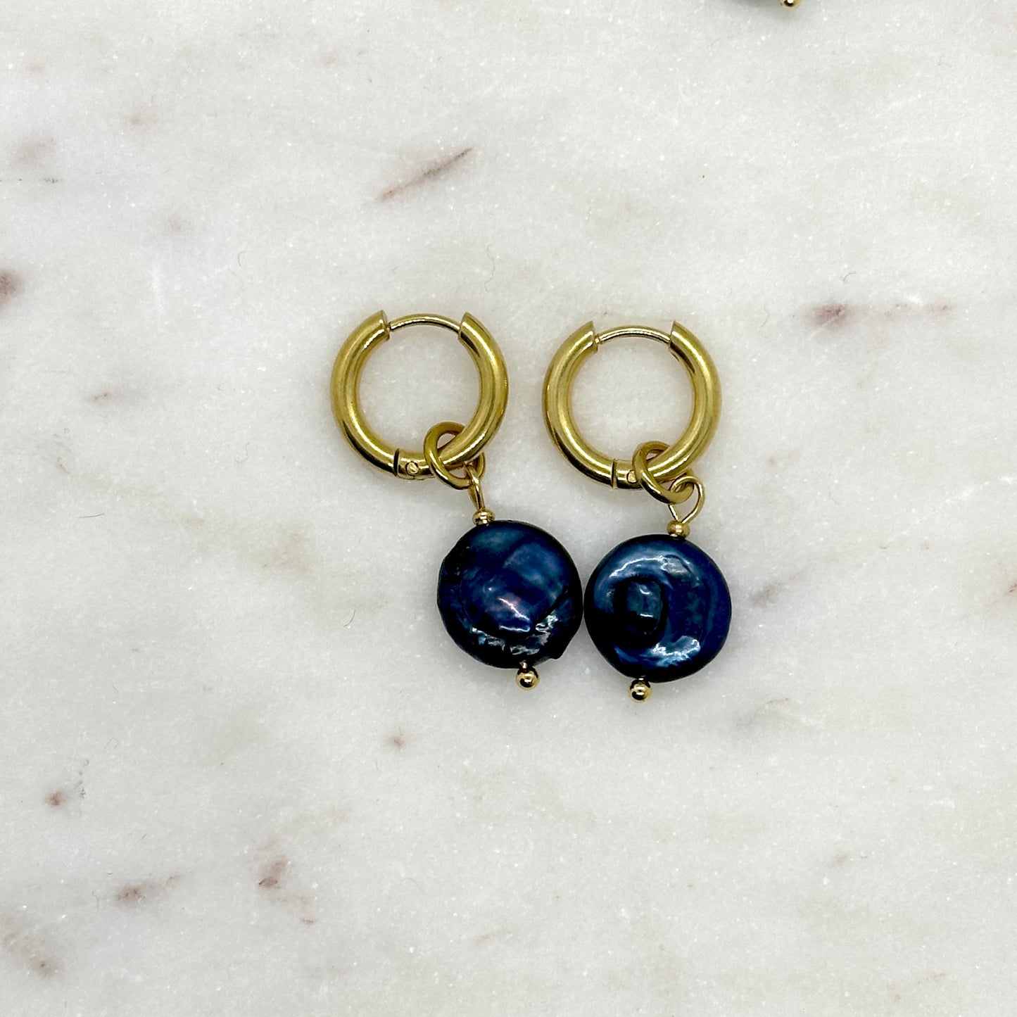 Gold hoop earrings with blue spherical pearl charms on a marble surface