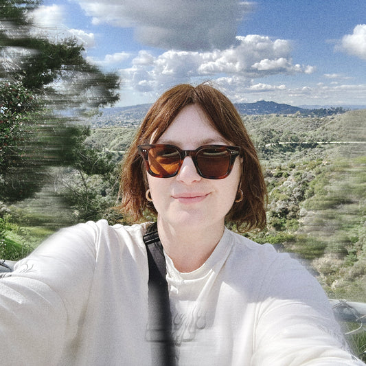 Person wearing sunglasses and gold chunky earrings with a scenic background of Los Angeles and the surrounding mountains.