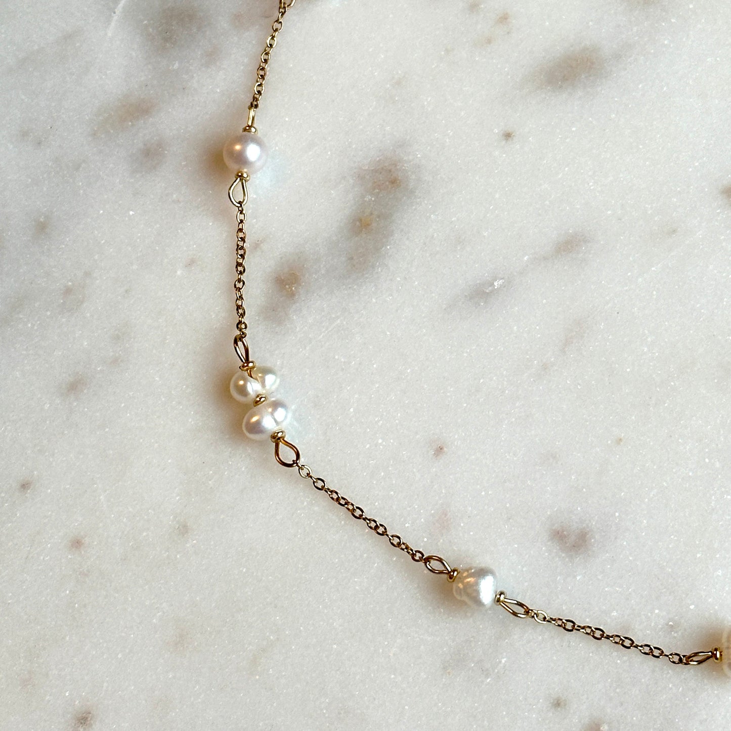 hadmade gold thin necklace with small upcycled pearls lying on a marble surface