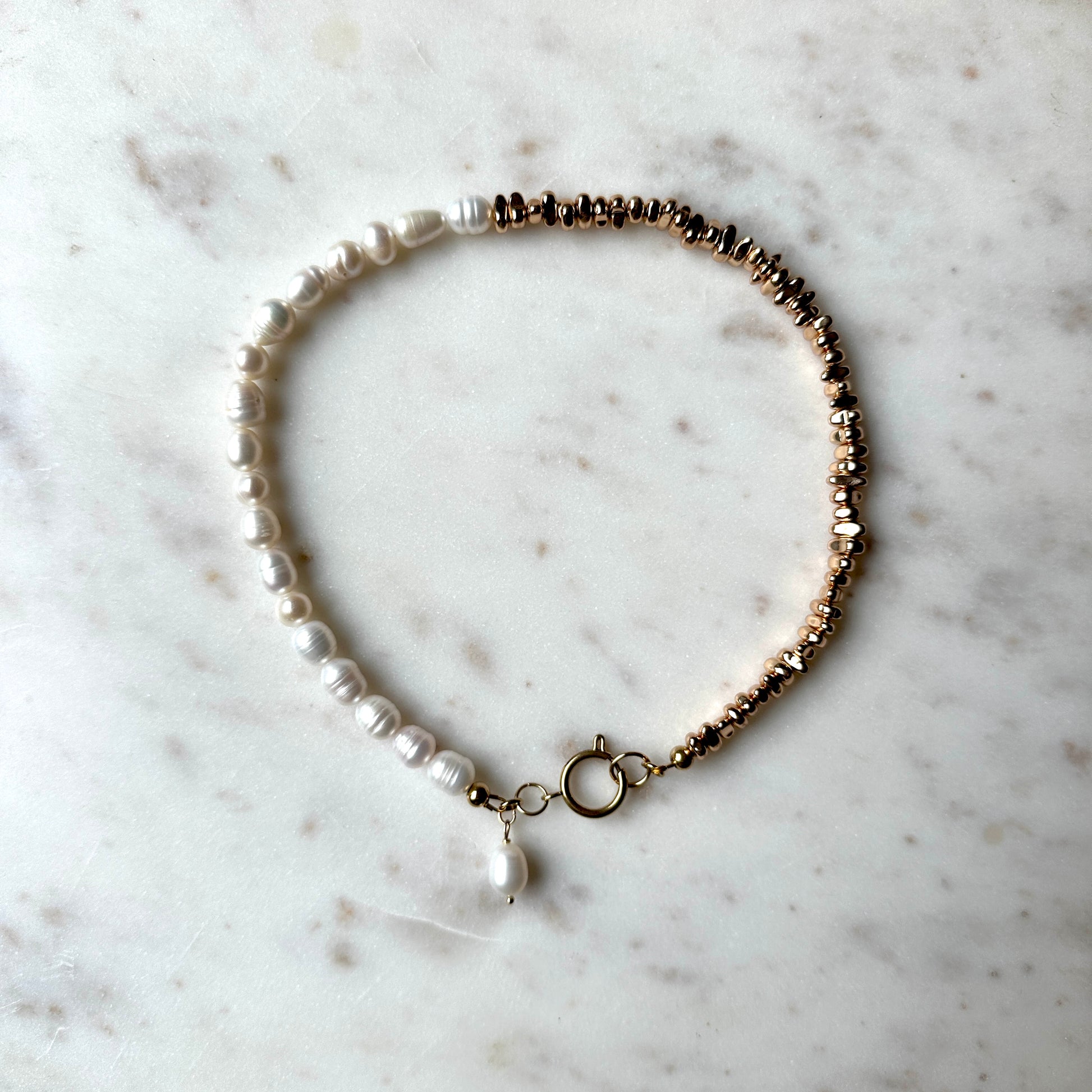 Handmade pearl necklace half with silver-plated hematite stones, and a hanging pearl pendant on a marble surface