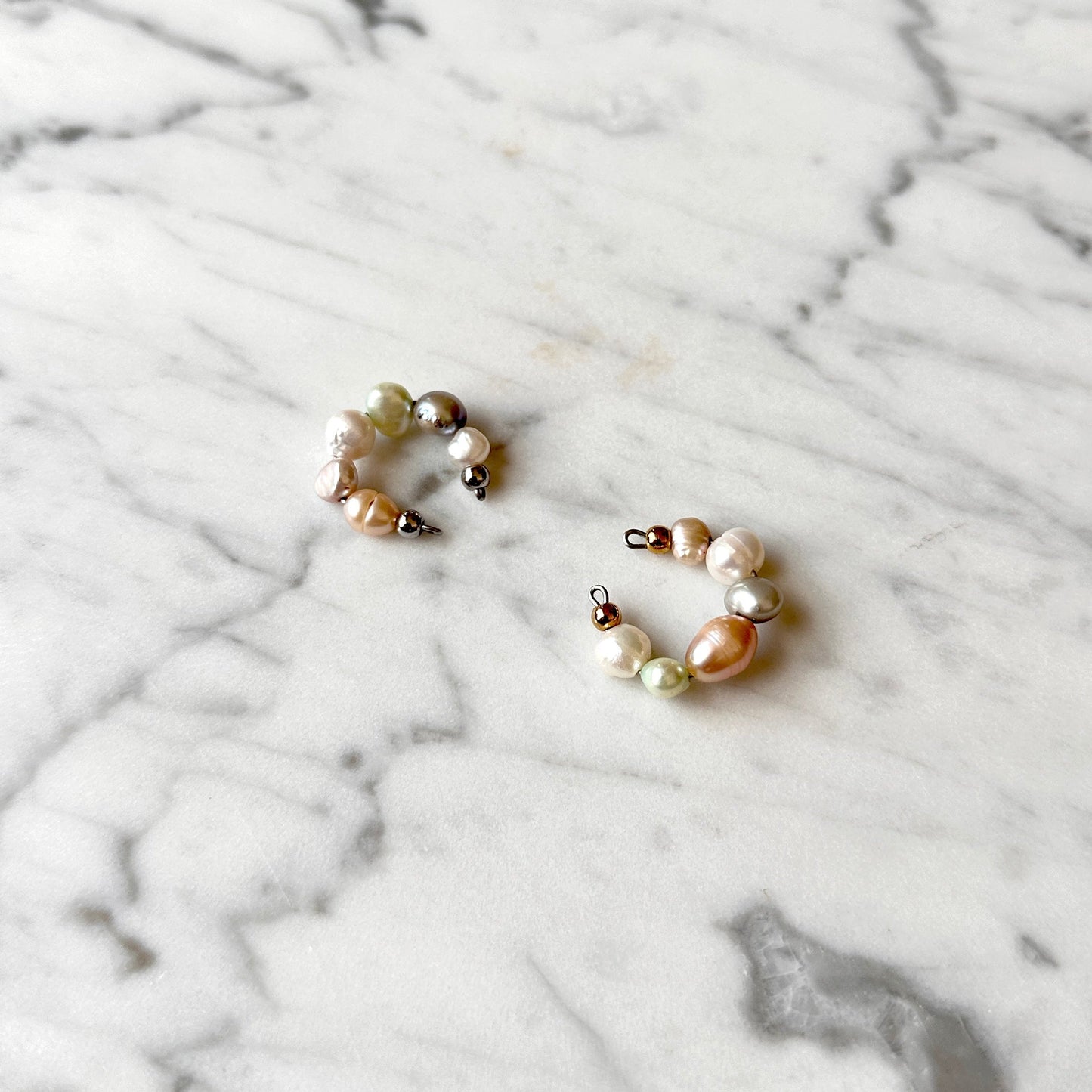 Two pearl cuff earrings on a marble surface