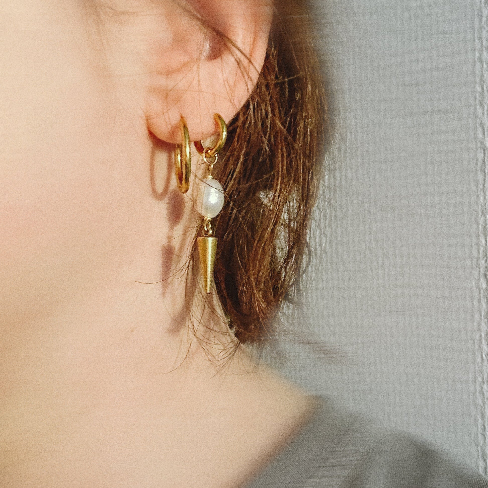 Gold hoop earrings with a pearl accent worn by a person against a neutral background