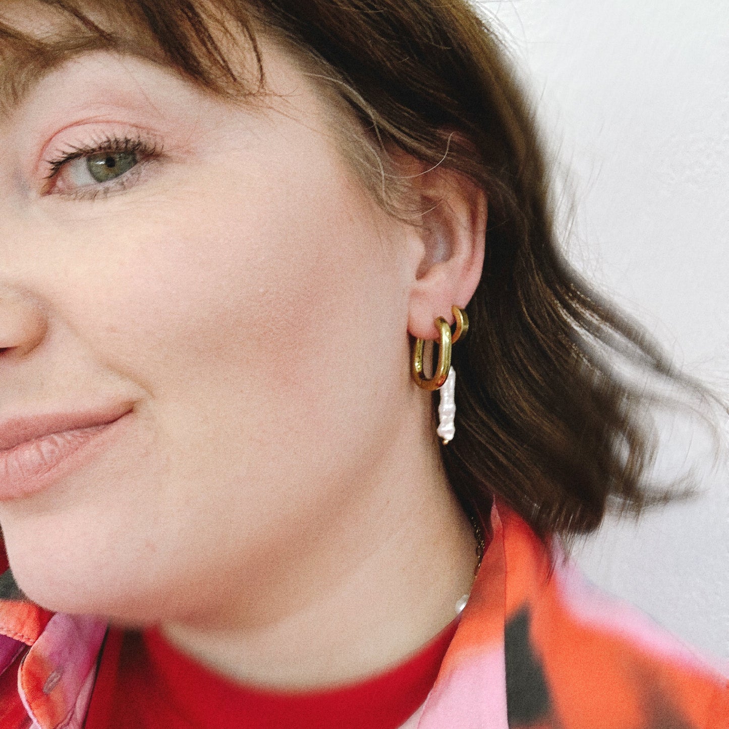 Close-up of a person wearing gold hoop earrings with a blurred background