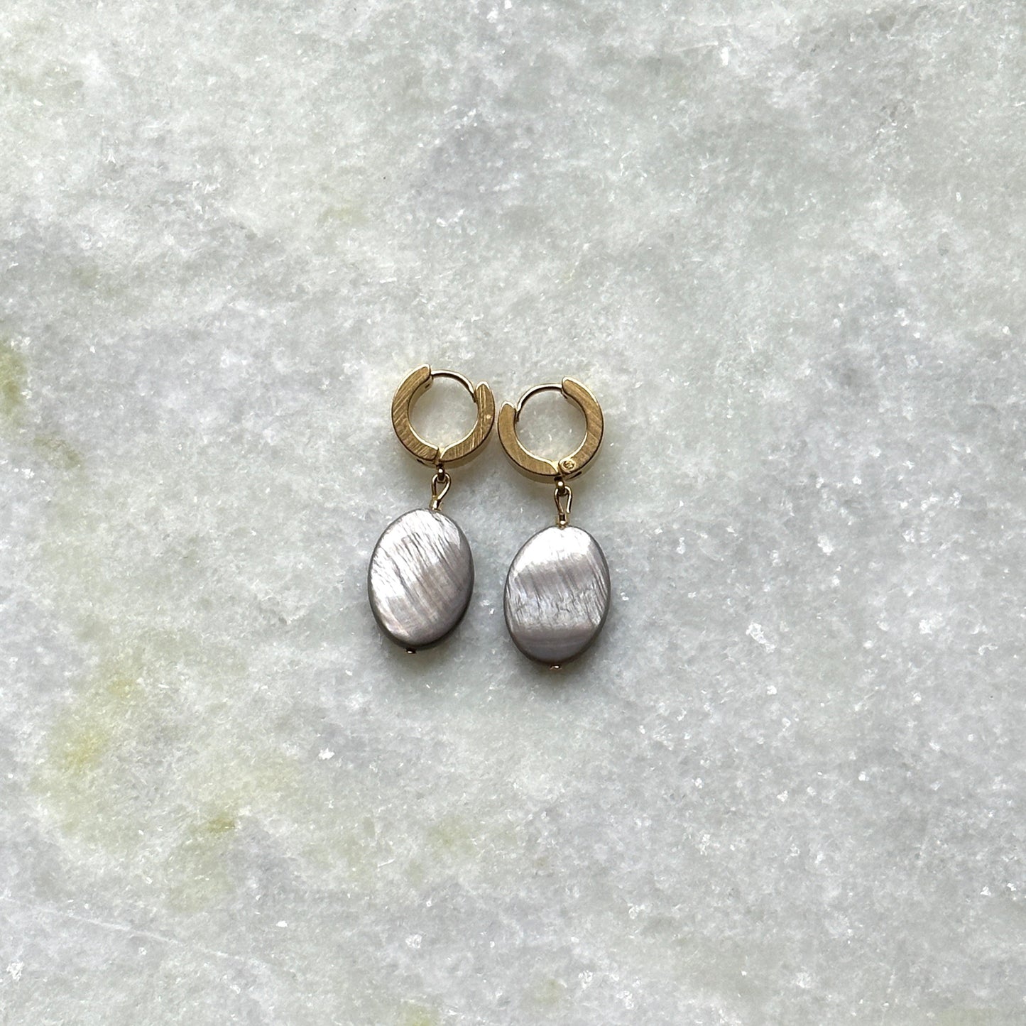 A pair of earrings in gold features mother-of-pearl pendants.
