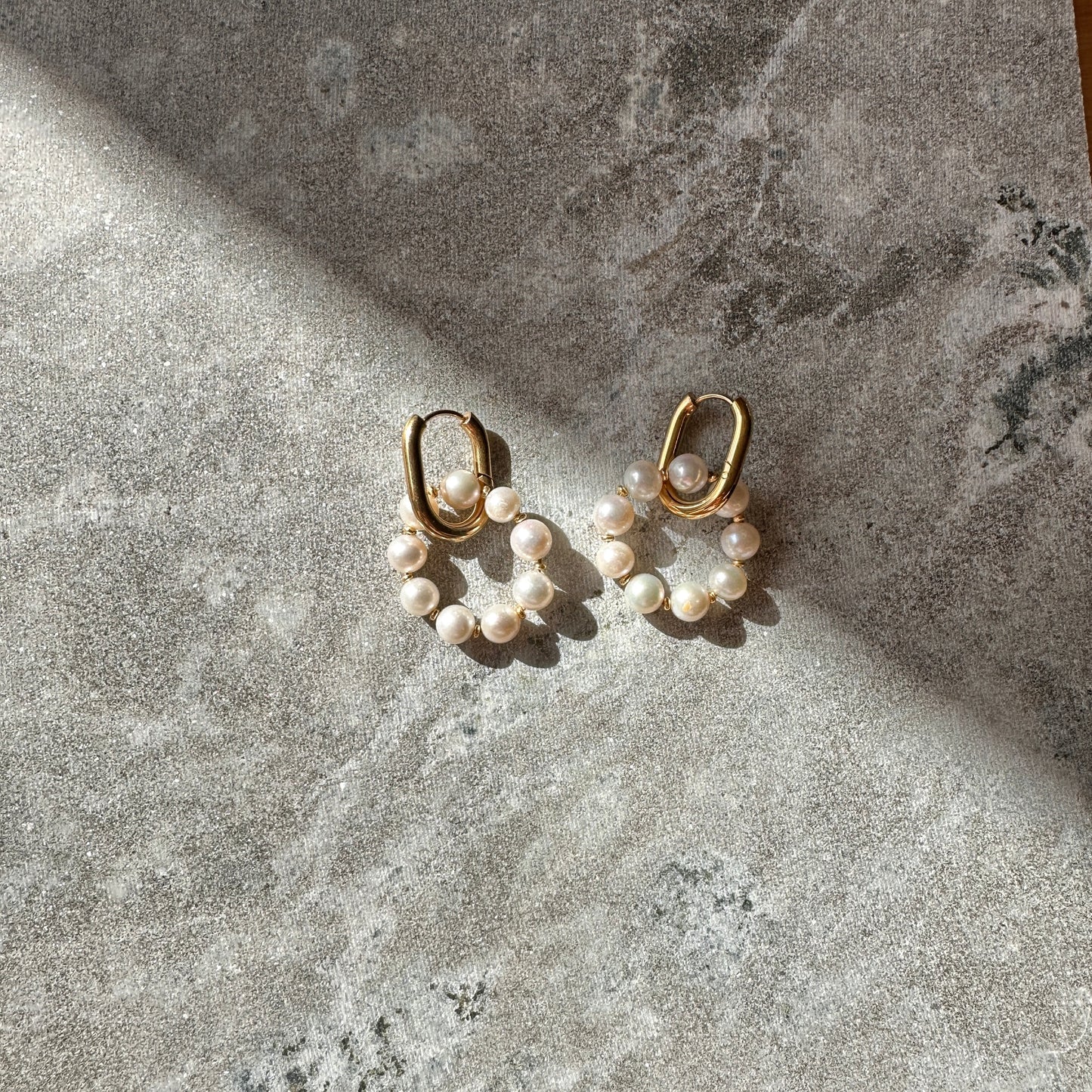 Pair of gold hoop earrings with pearl beads on a textured stone surface