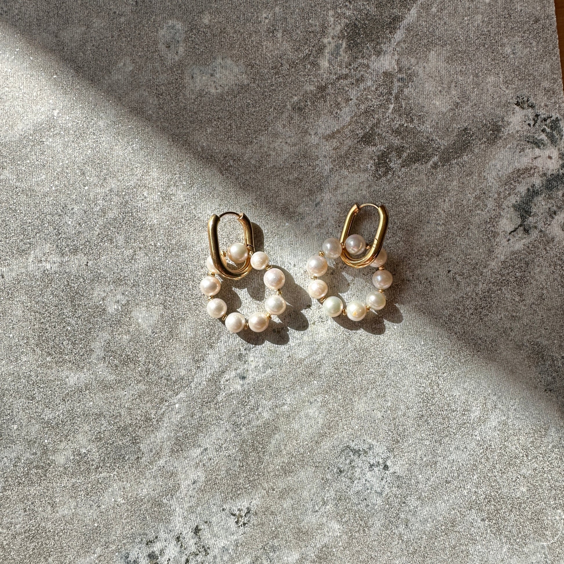 Pair of gold hoop earrings with pearl beads on a textured stone surface