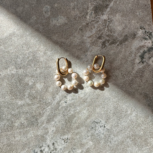 Pair of gold hoop earrings with pearl beads on a textured stone surface