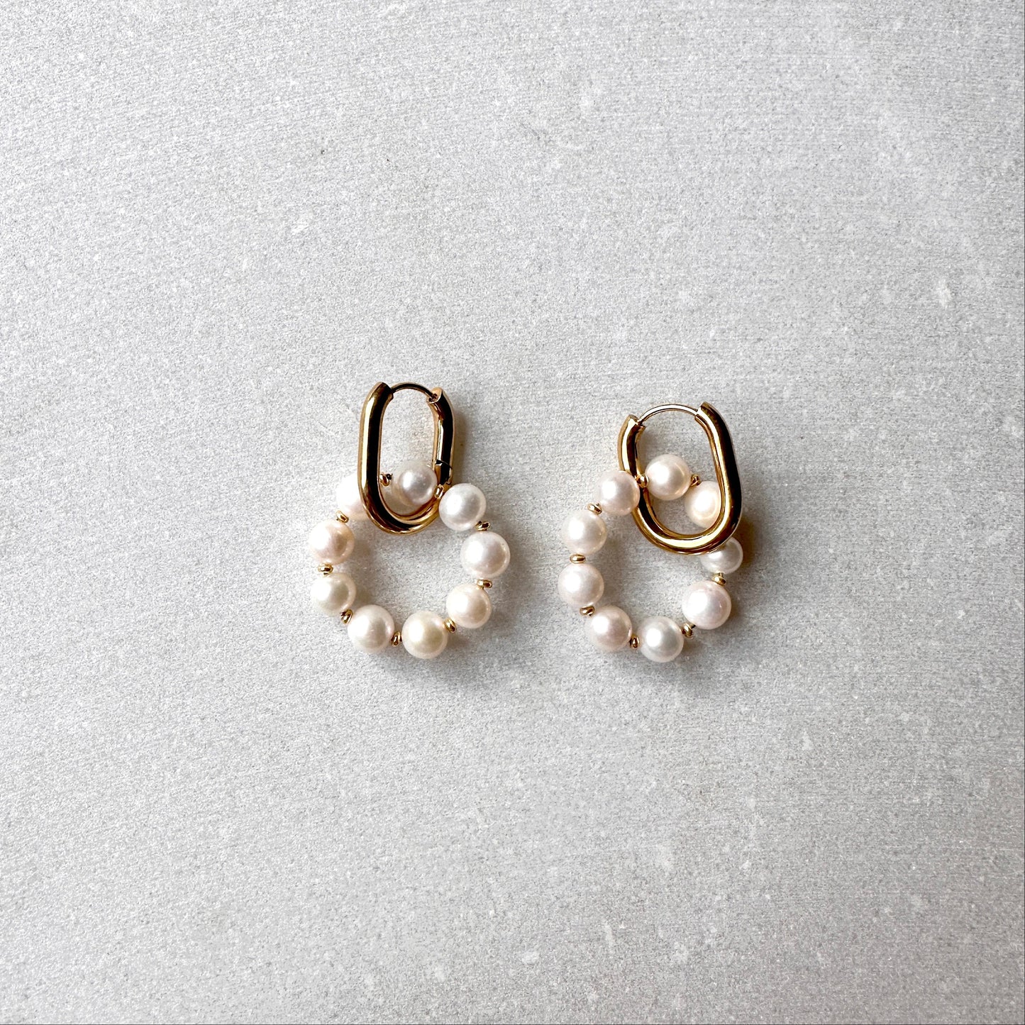 Pair of pearl earrings with gold hooks on a light gray background