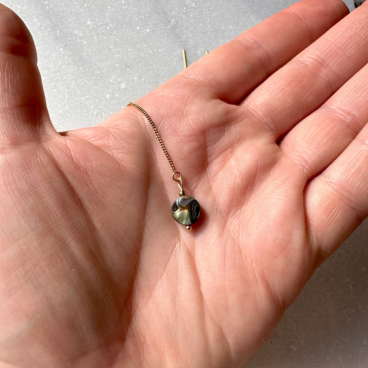 A small gold chain necklace with an iridescent green and black bead pendant resting on an open hand.