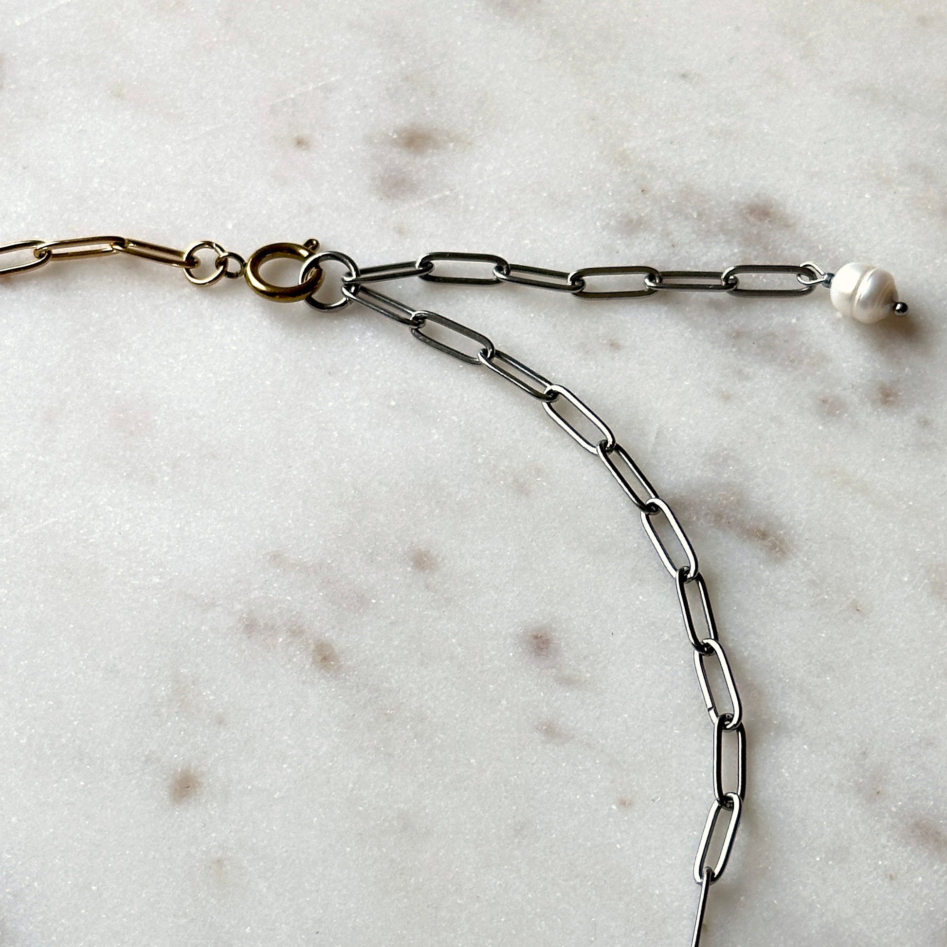 Silver chain necklace with a pearl on a marble surface