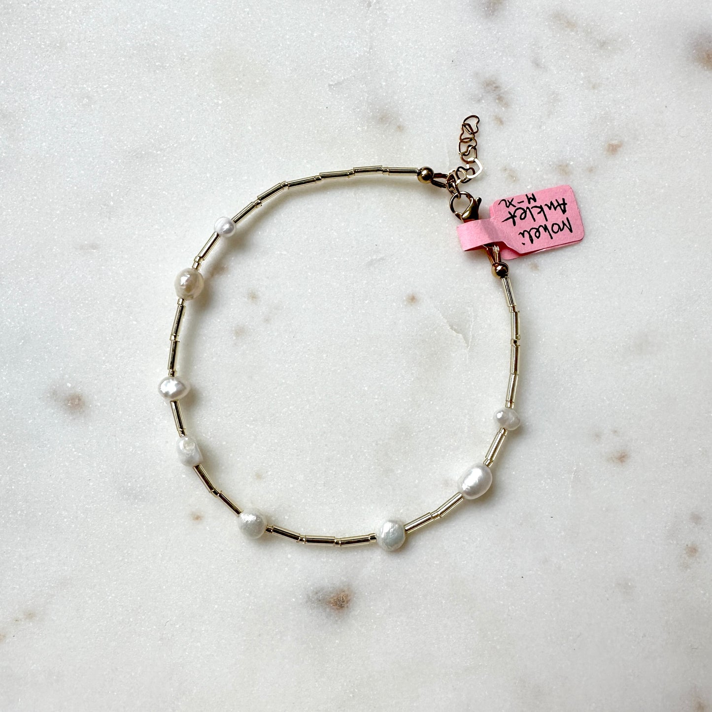 a pearl and glass bead anklet on a stainless steel wire, laid out on a marble surface.