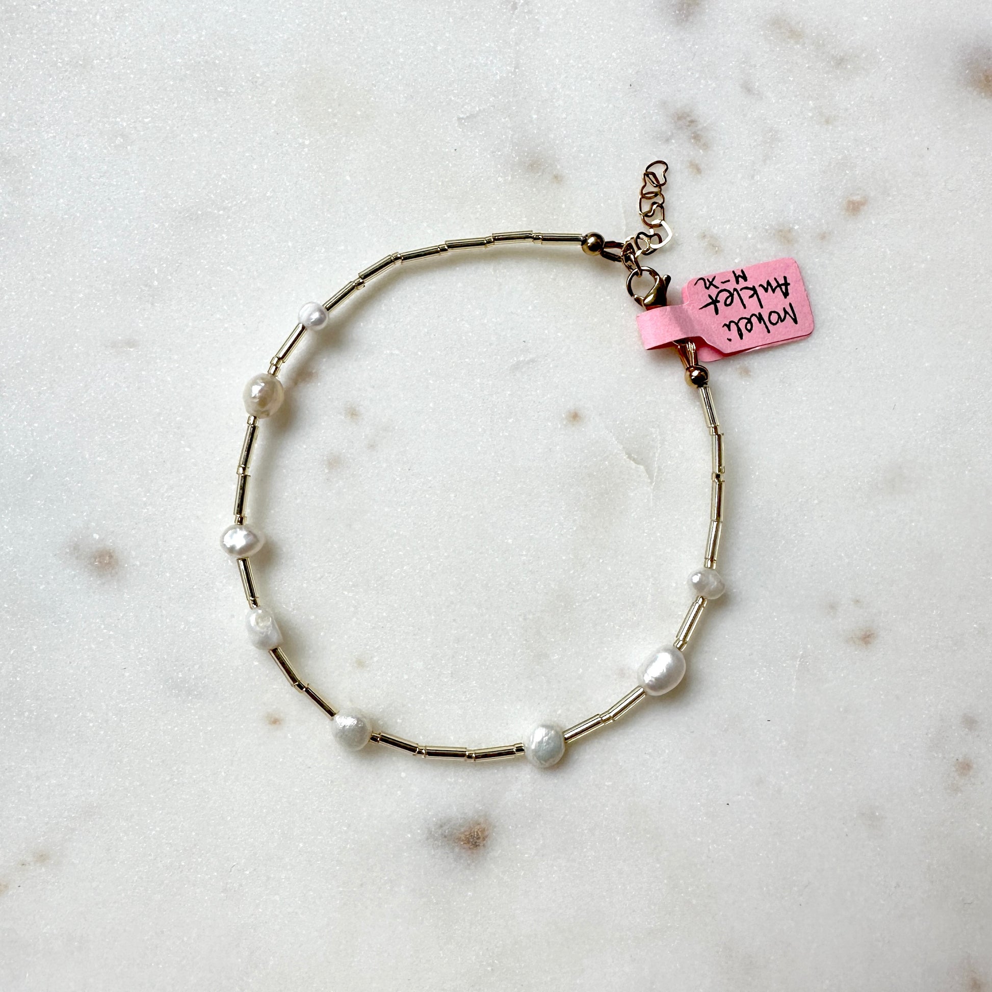 a pearl and glass bead anklet on a stainless steel wire, laid out on a marble surface.
