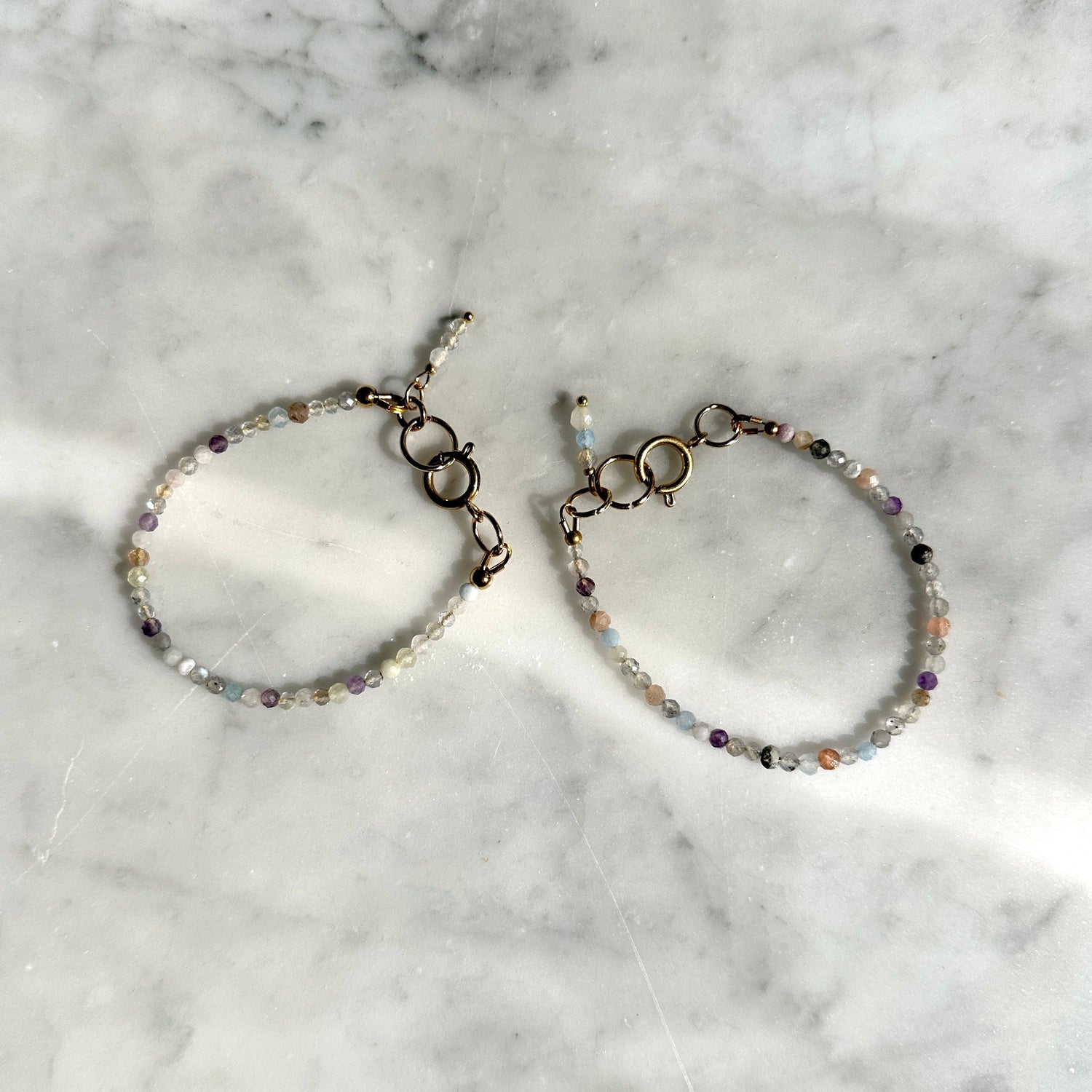 Pair of handmade bracelets of micro-stones and crystals on a marble surface