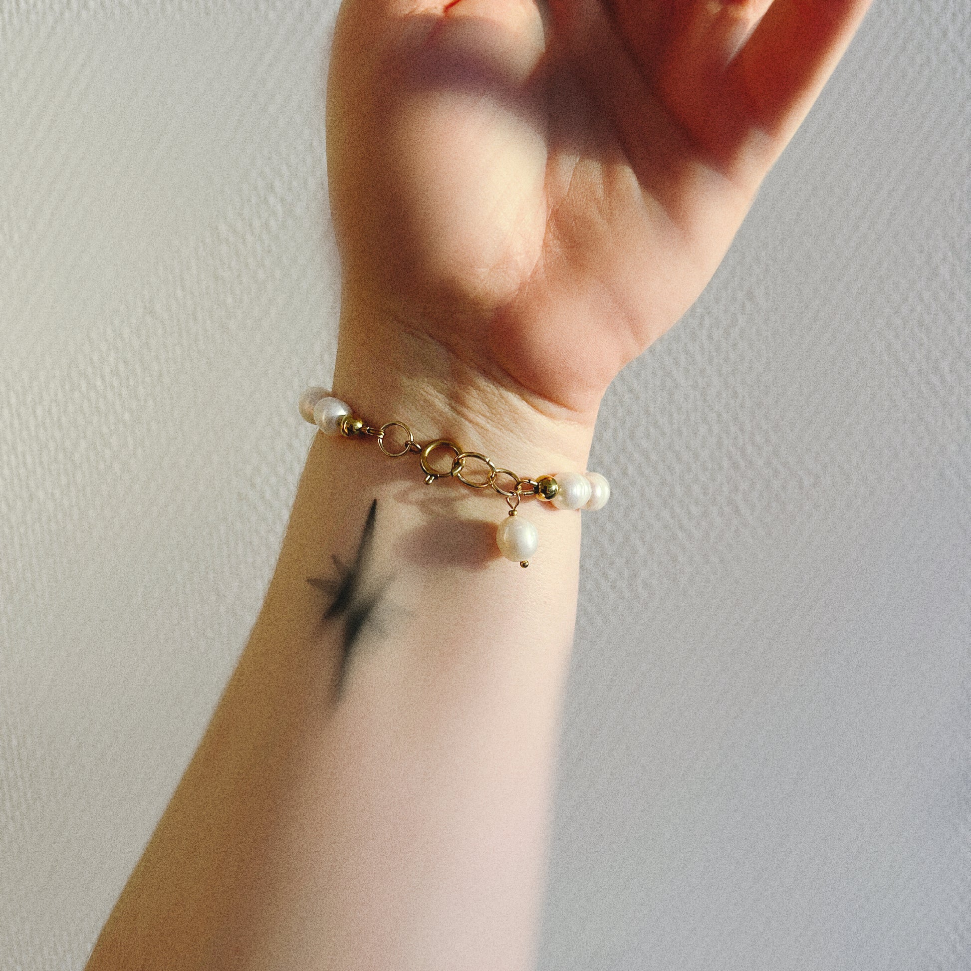 Hand wearing a pearl bracelet with a gold clasp on a neutral background