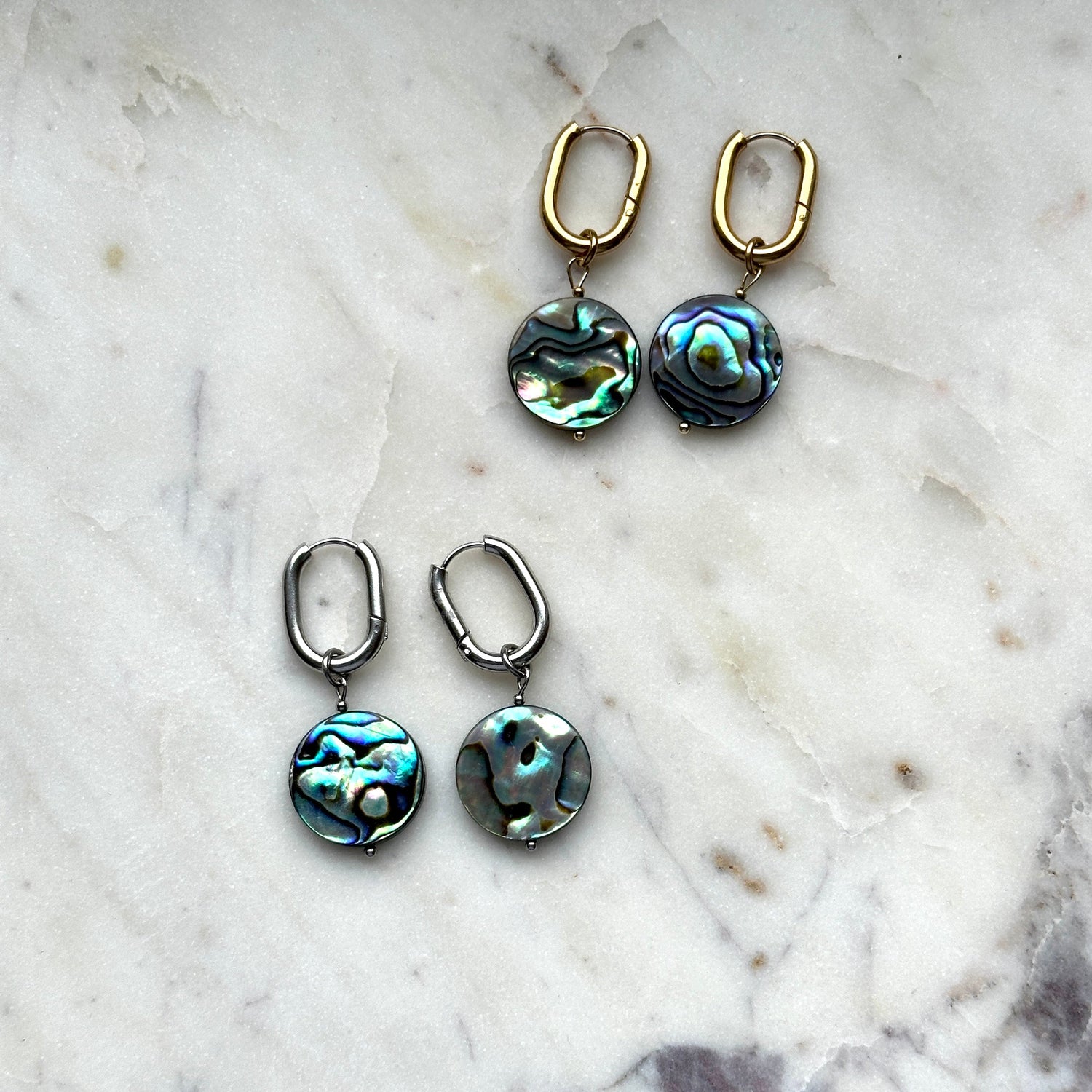 handmade earrings of abalone shell lying on a white marble background 