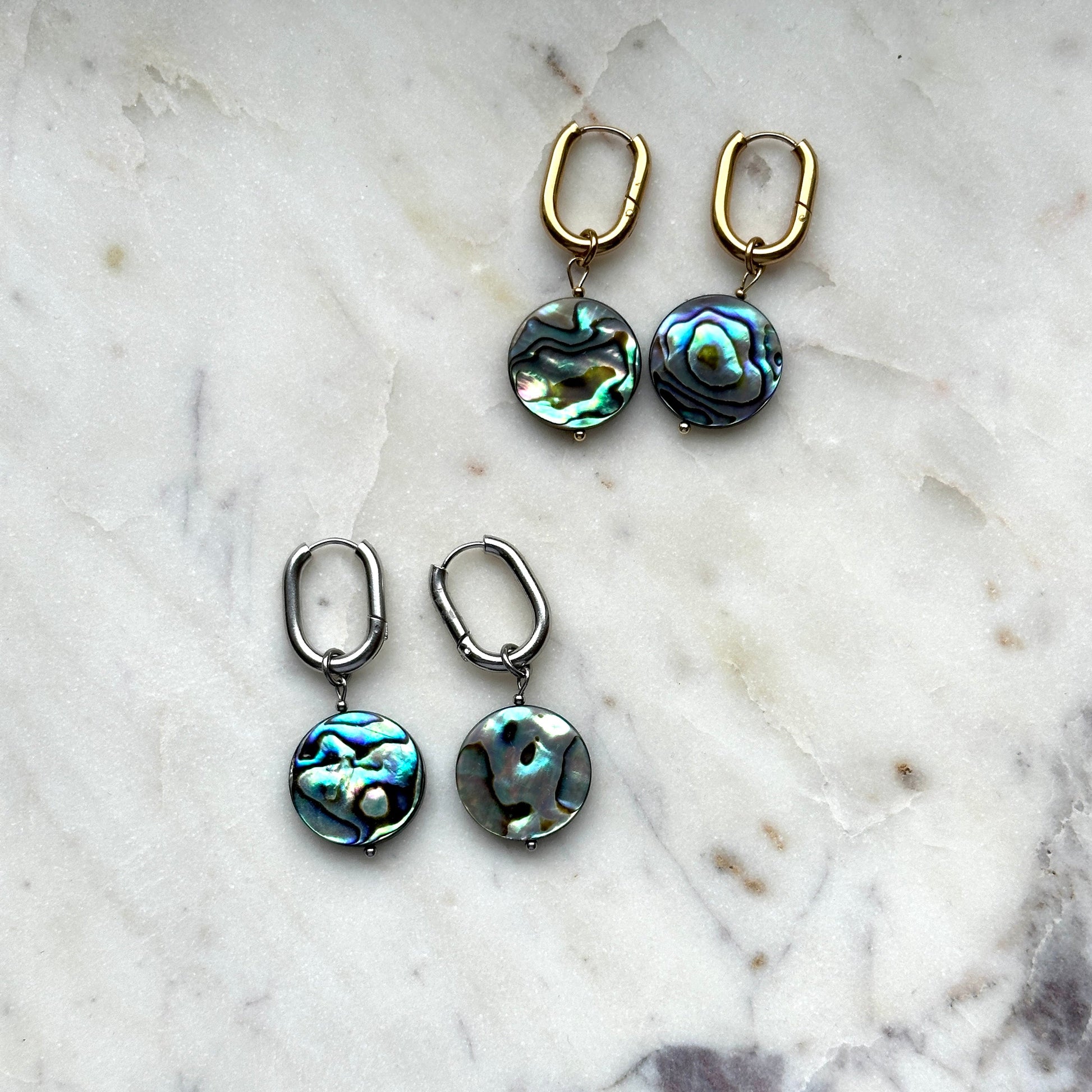 handmade earrings of abalone shell lying on a white marble background 