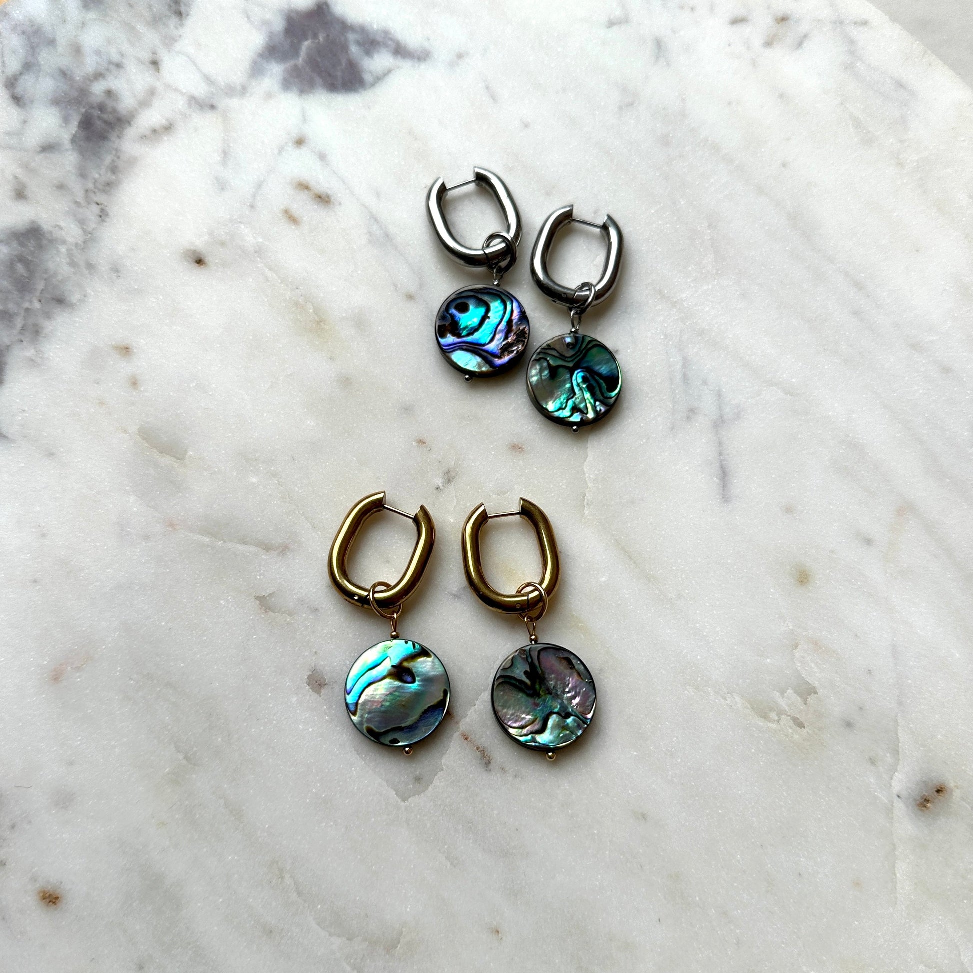 Pair of earrings with abalone shell drops on a marble surface