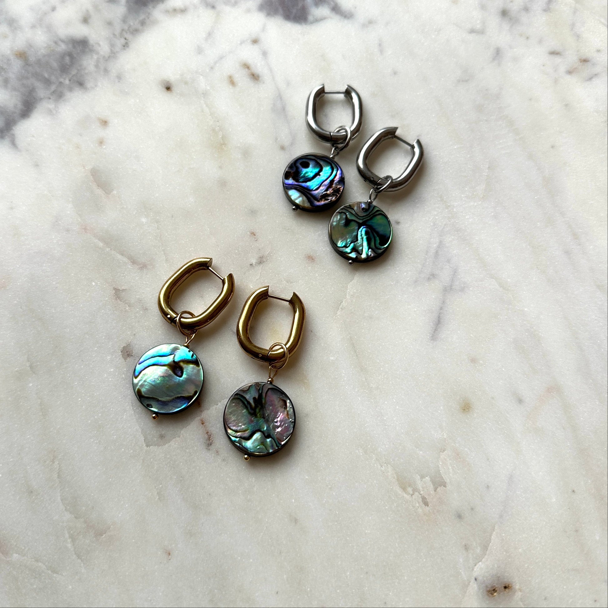 Pair of earrings with abalone shell drops on a marble surface