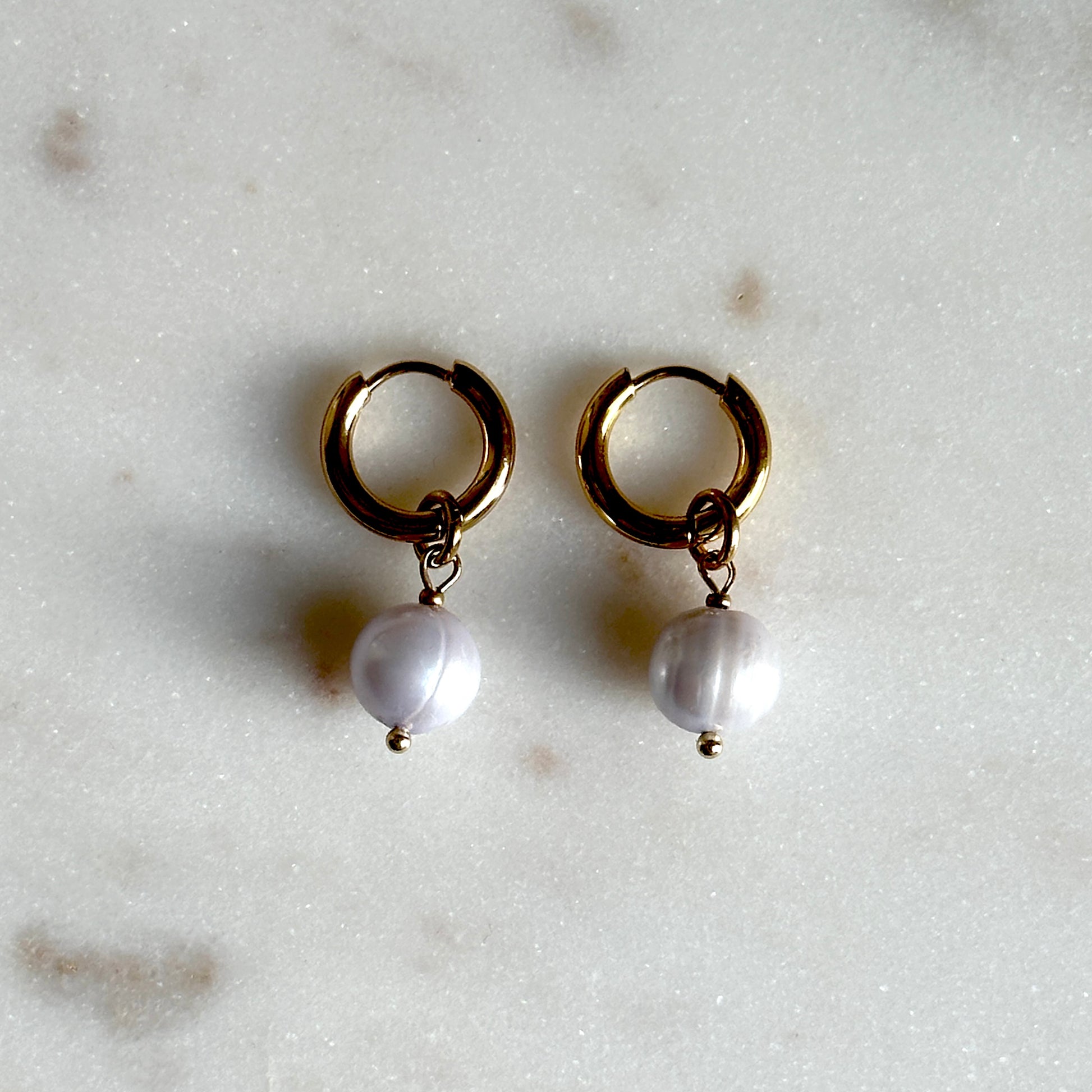 Gold hoop earrings with pearl drops on a light marble background