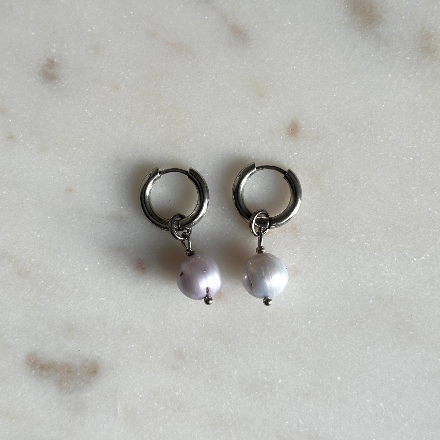 Pair of small hoop earrings with pearl drops on a light marble background