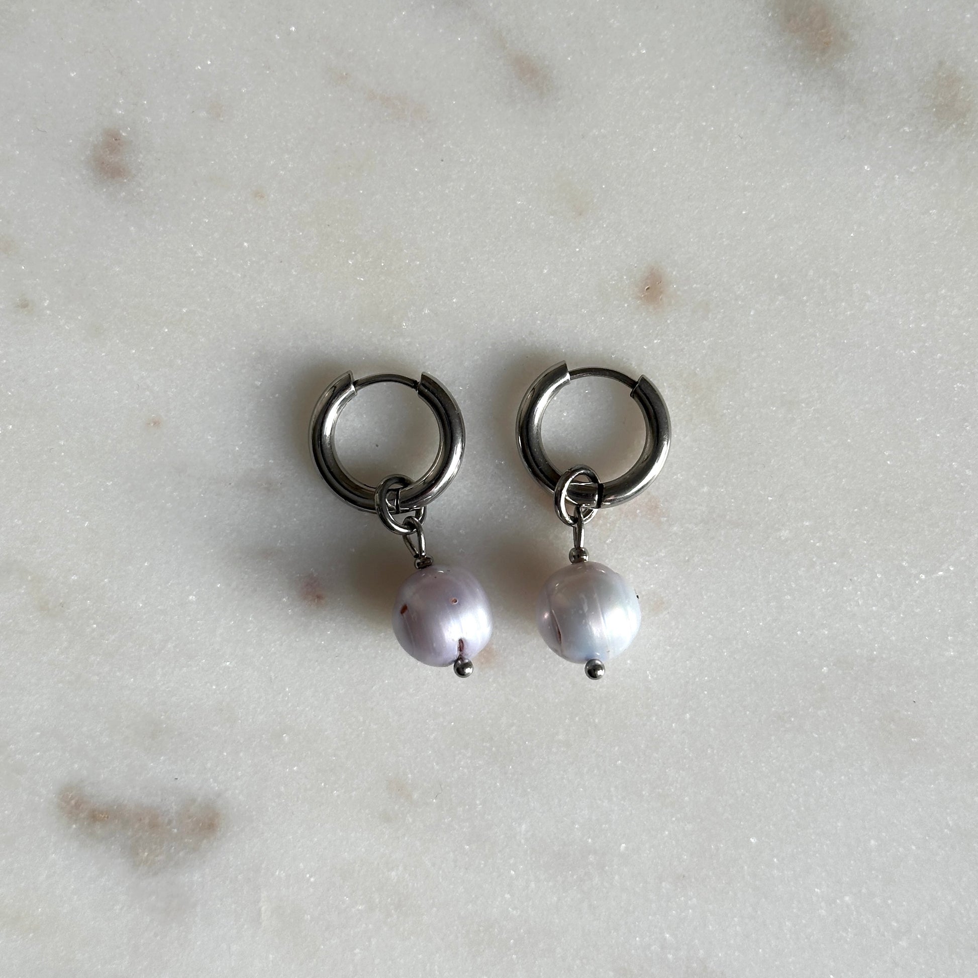 Pair of small hoop earrings with pearl drops on a light marble background