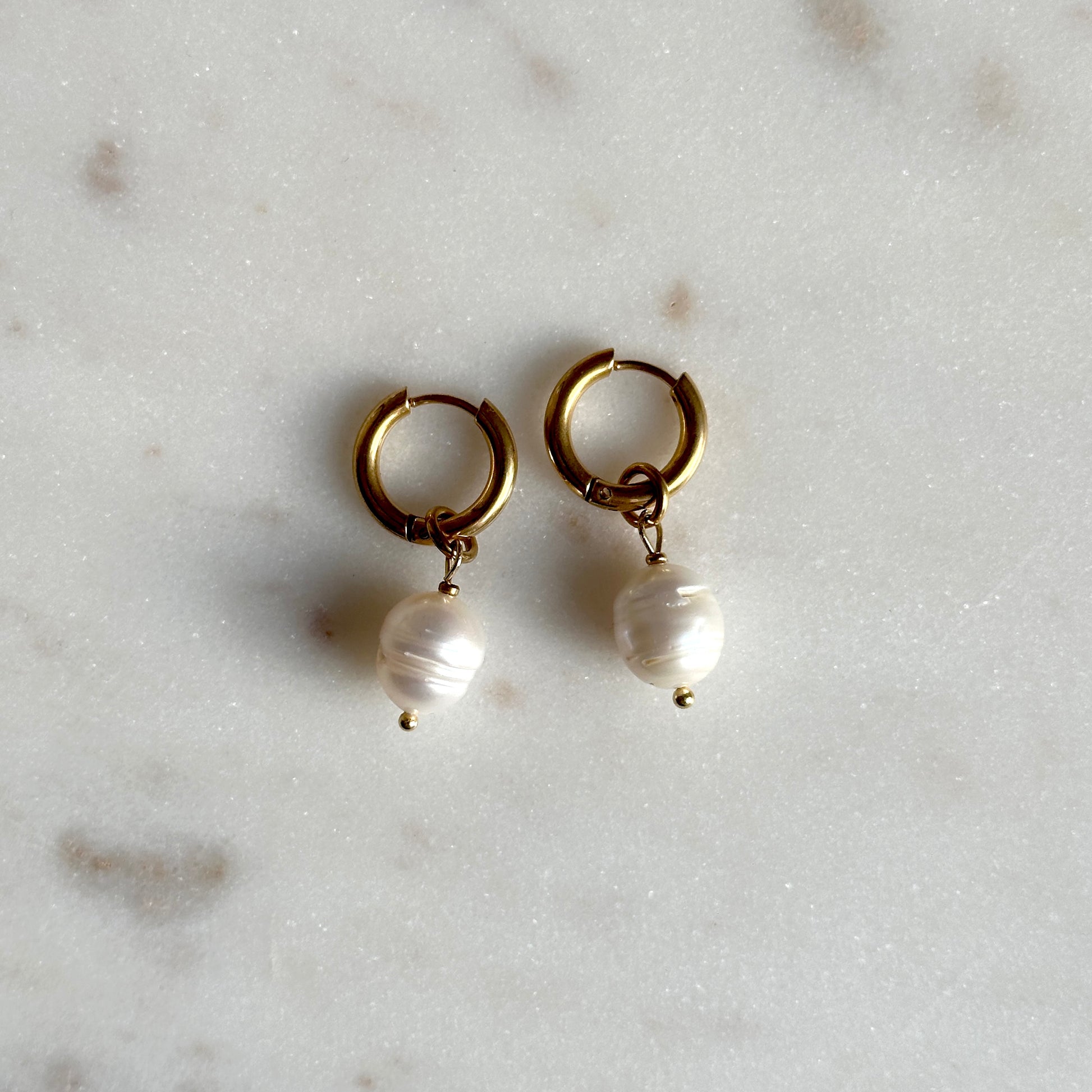 Gold hoop earrings with pearl drops on a light gray surface