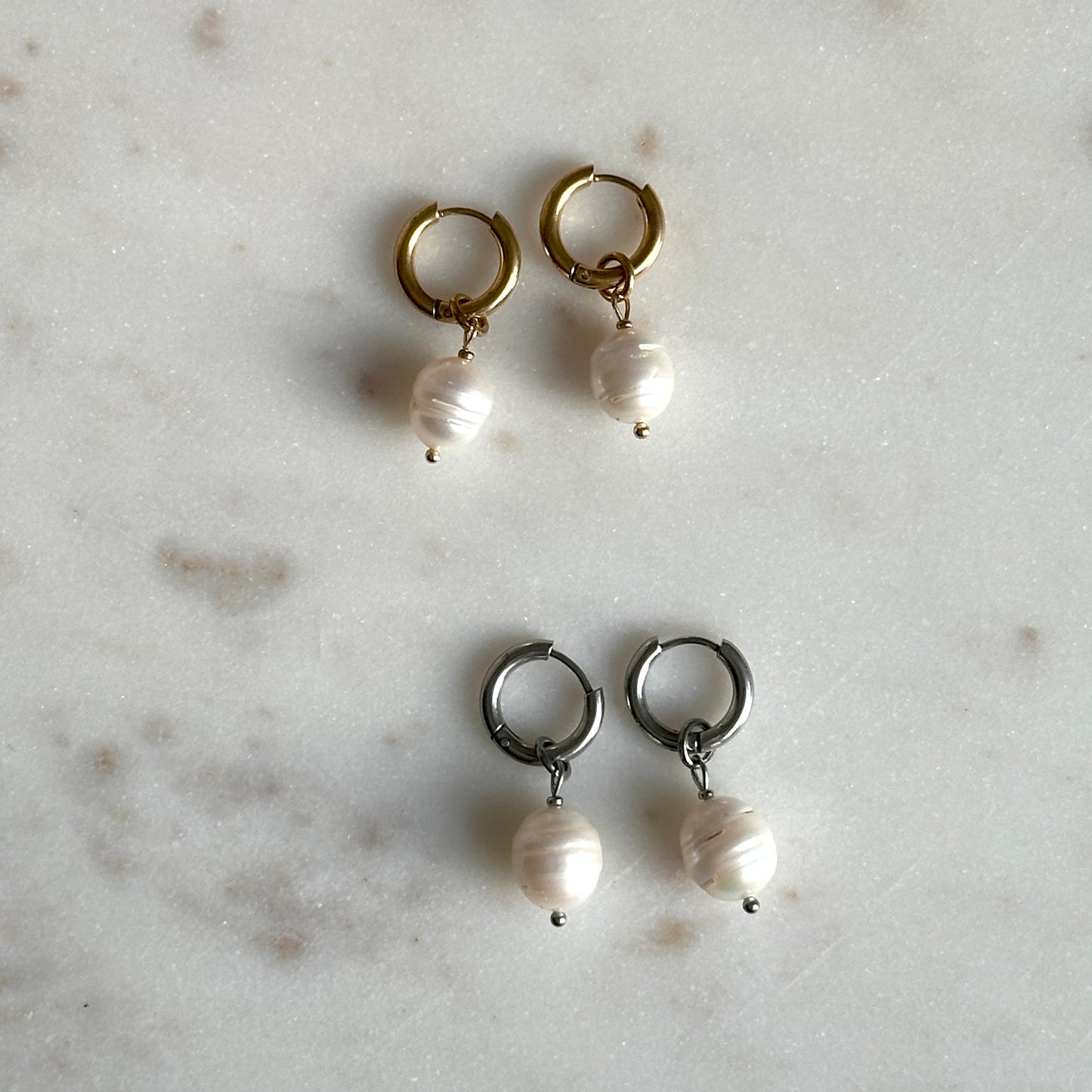 Pair of hoop earrings with pearl drops on a light gray surface