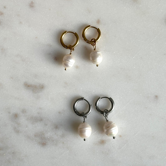Pair of hoop earrings with pearl drops on a light gray surface