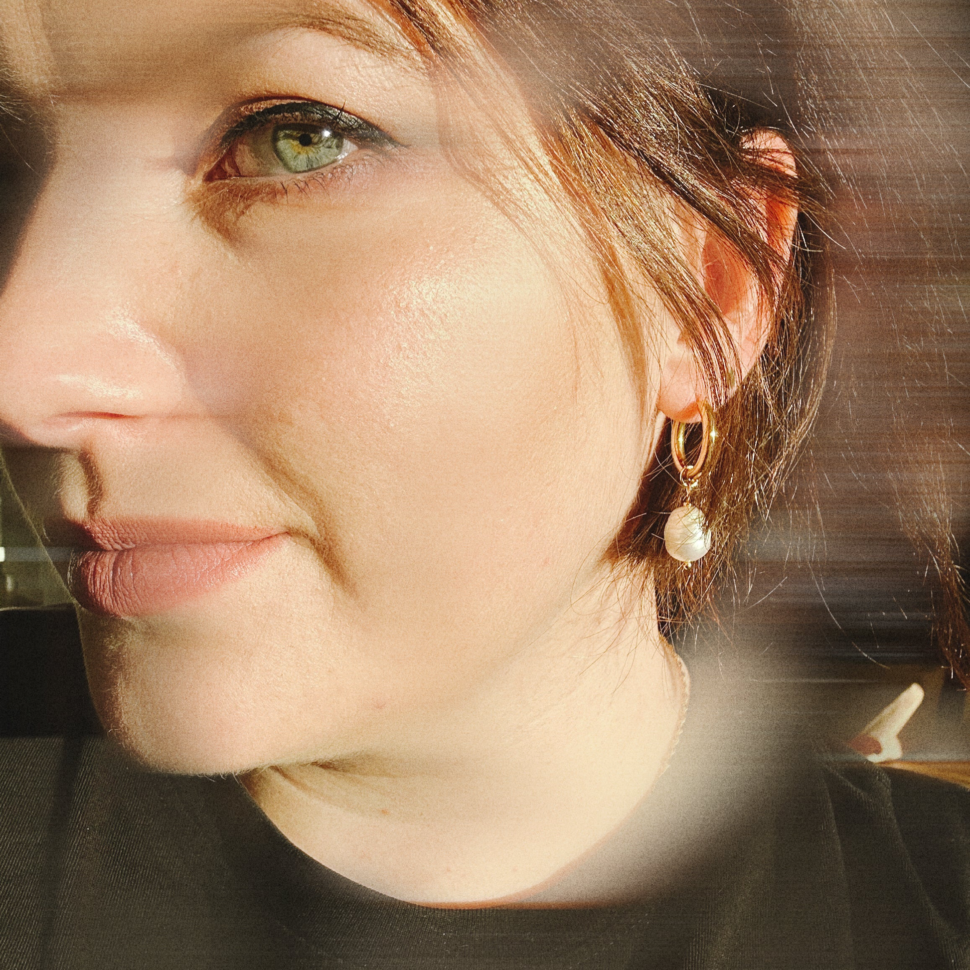 Close-up of a person wearing gold hoop earrings with a blurred background