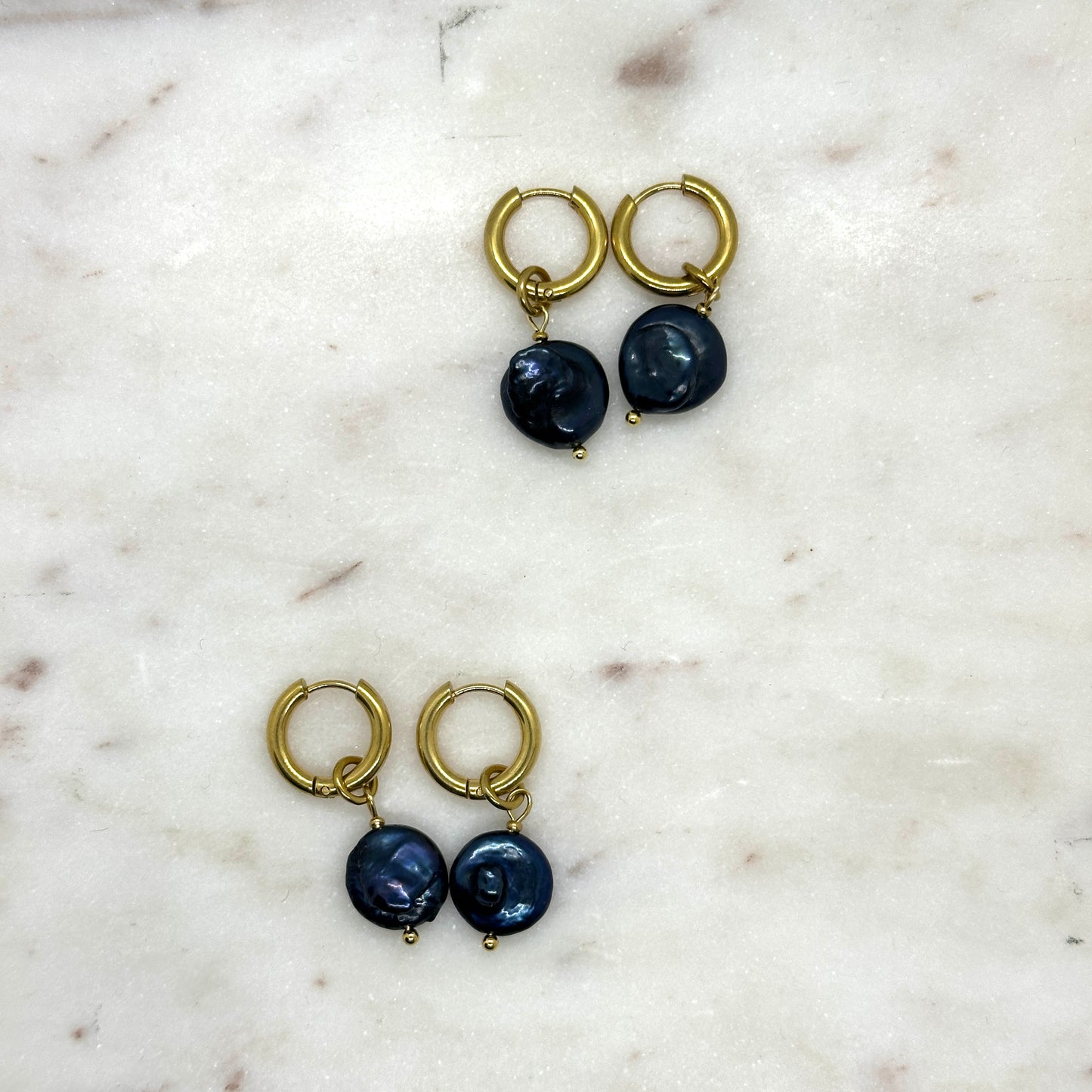Pair of gold hoop earrings with dark blue pearls on a marble surface