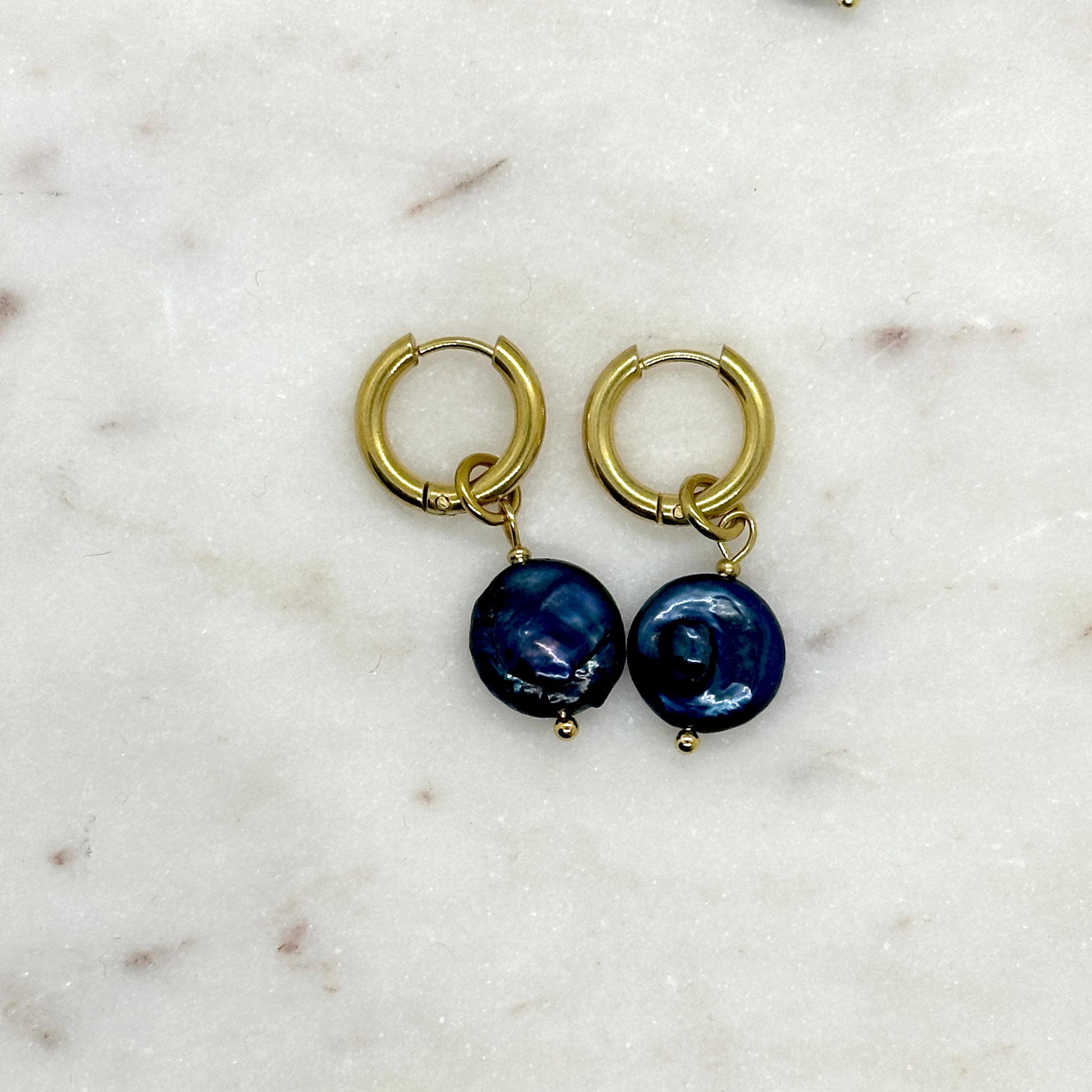 Gold hoop earrings with blue spherical pearl charms on a marble surface