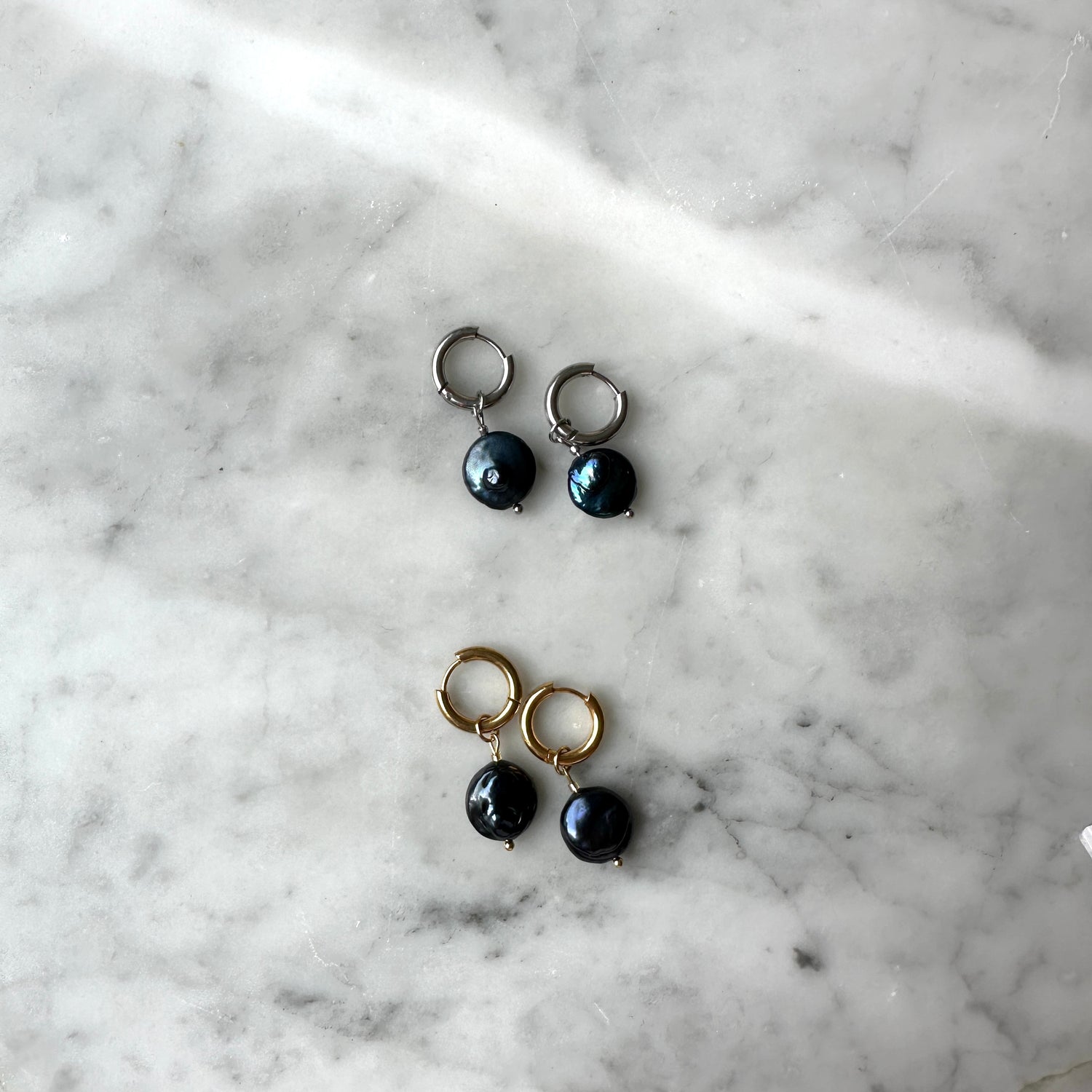 Pair of earrings with black pearls on a marble surface