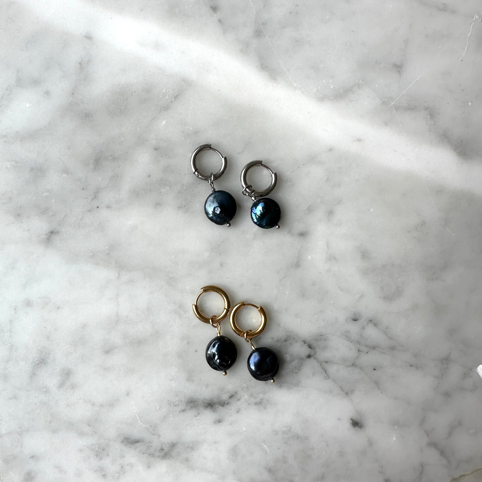 Pair of earrings with black pearls on a marble surface