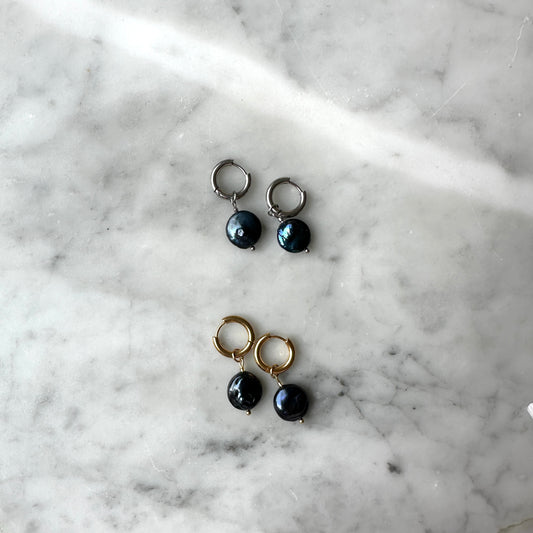 Pair of earrings with black pearls on a marble surface