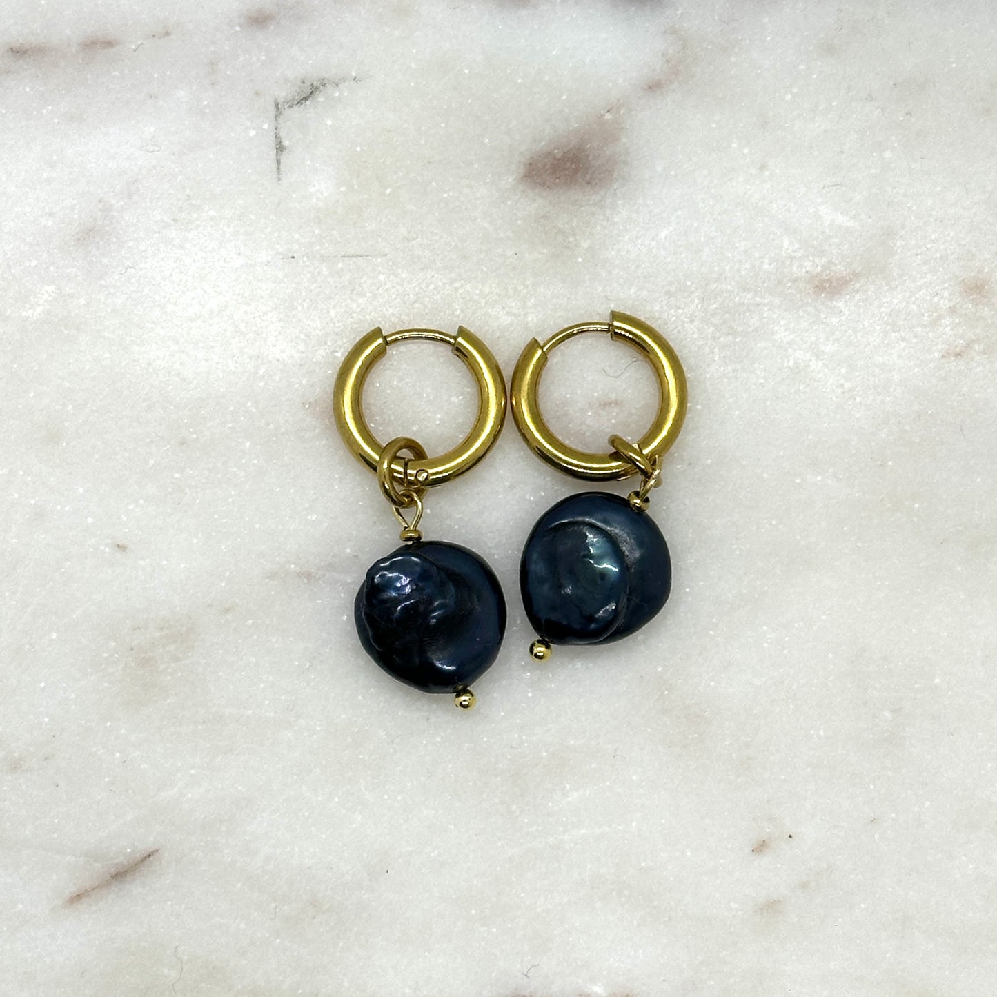 Pair of gold hoop earrings with black pears on a marble surface